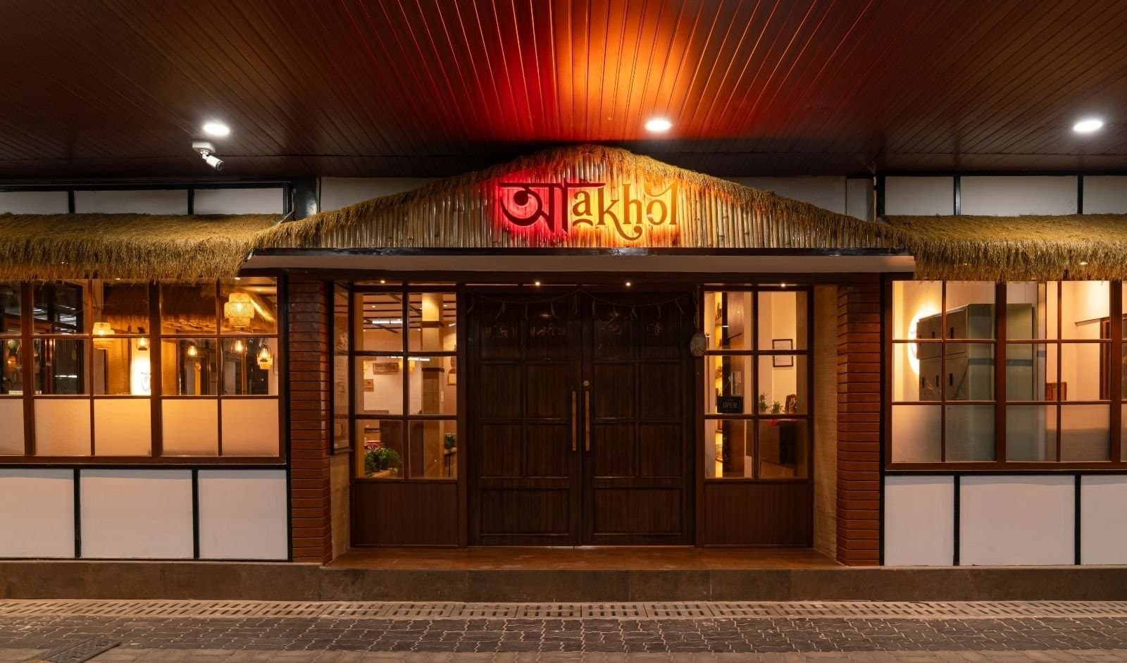 Night exterior of Aakhol in Hyderabad, with thatched awning and lit Assamese-script signage
