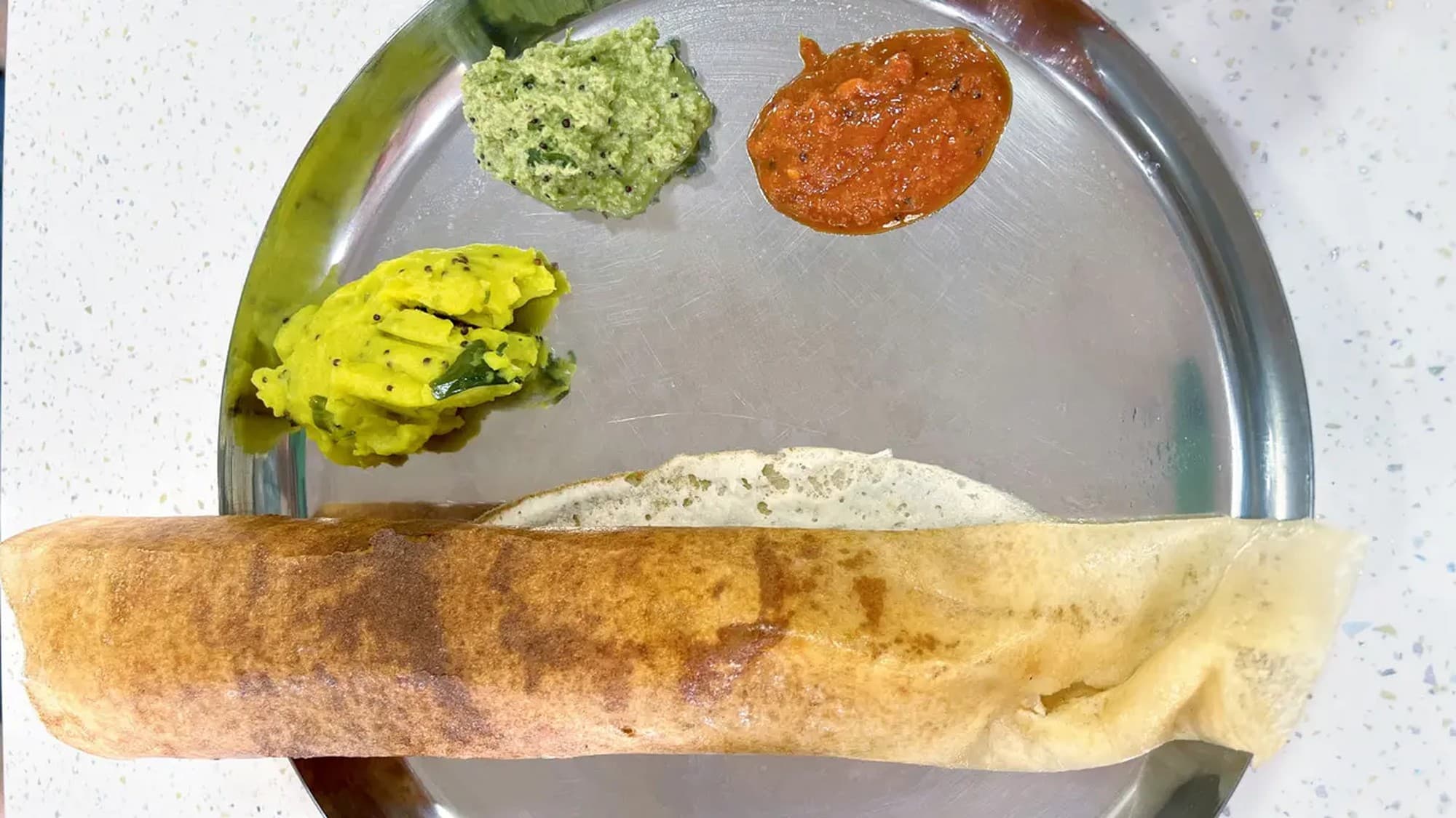 Rolled masala dosa on a steel plate with potato masala, green chutney, and red chutney at &Chutney in Pune