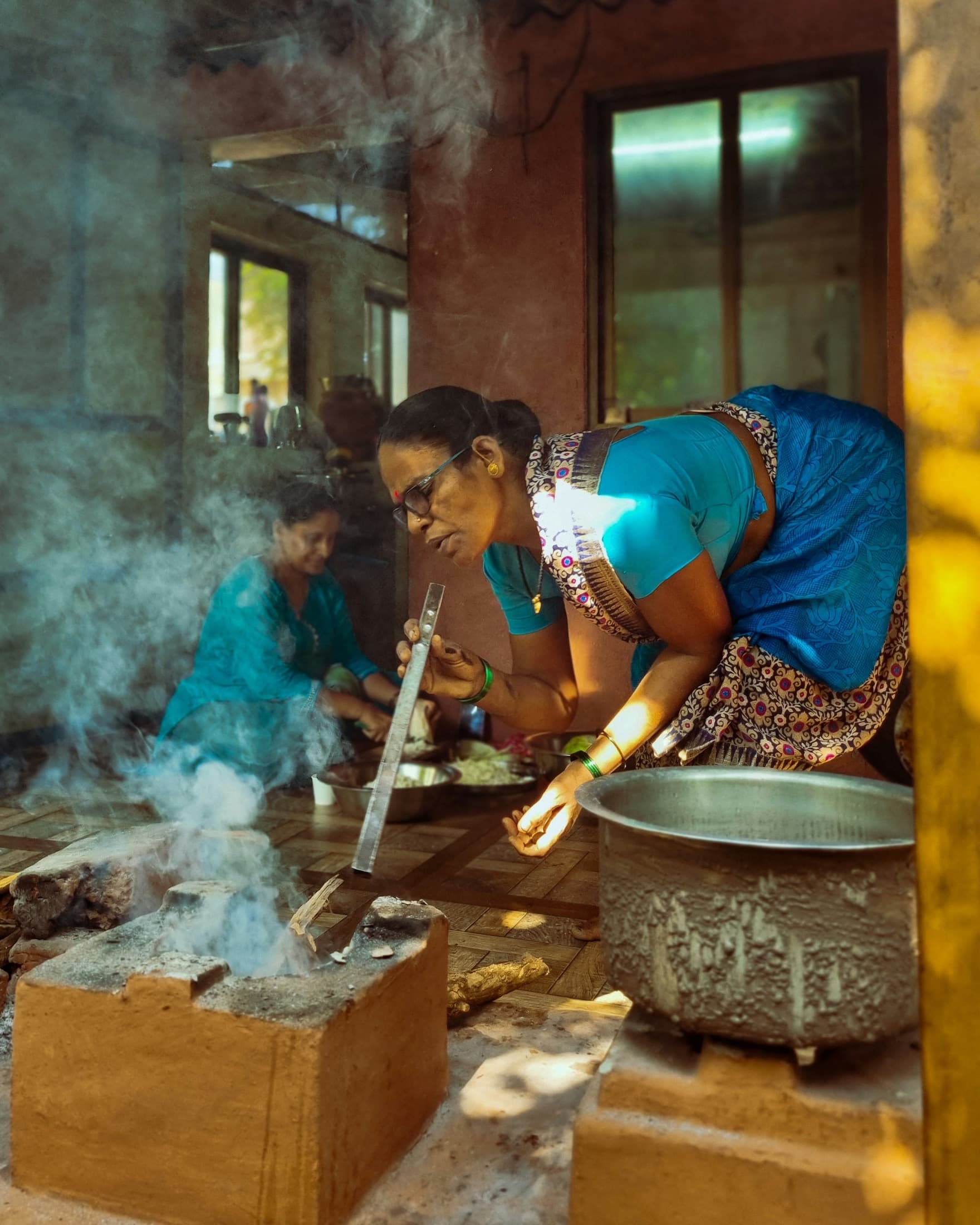 A woman tending a wood-fired chulha in a traditional kitchen in Ratnagiri, Maharashtra