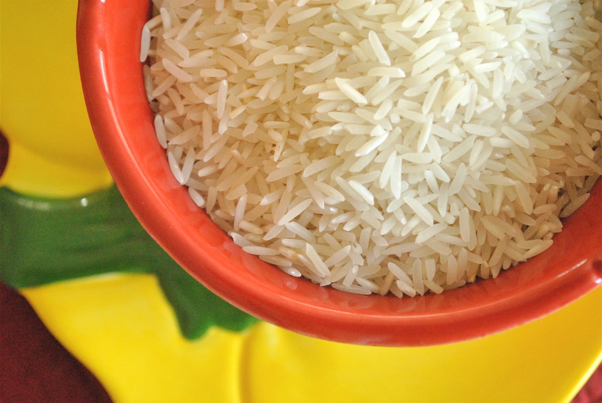Uncooked long-grain basmati rice piled in a red bowl