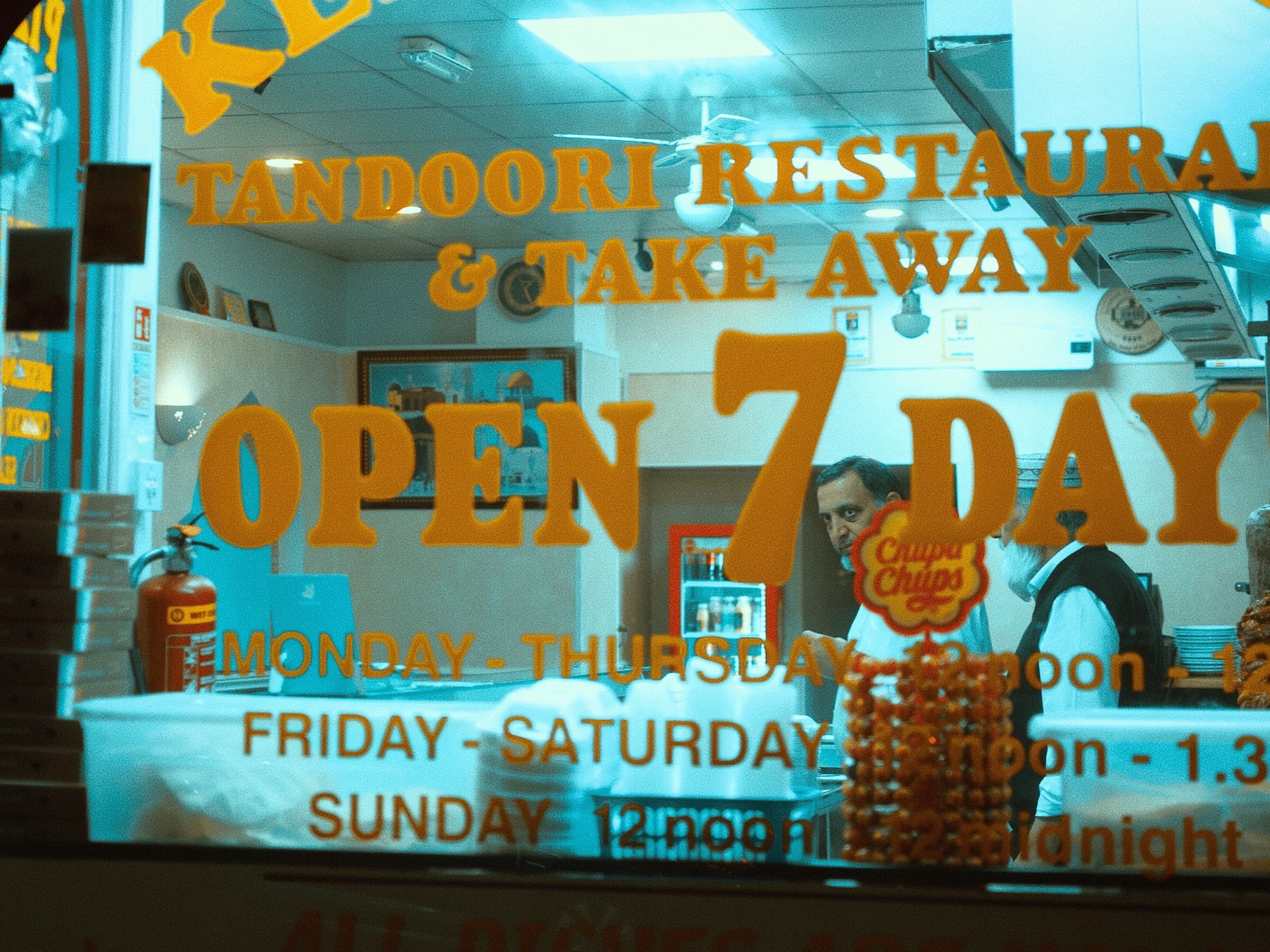 Night view through a tandoori restaurant and takeaway window with OPEN 7 DAYS lettering