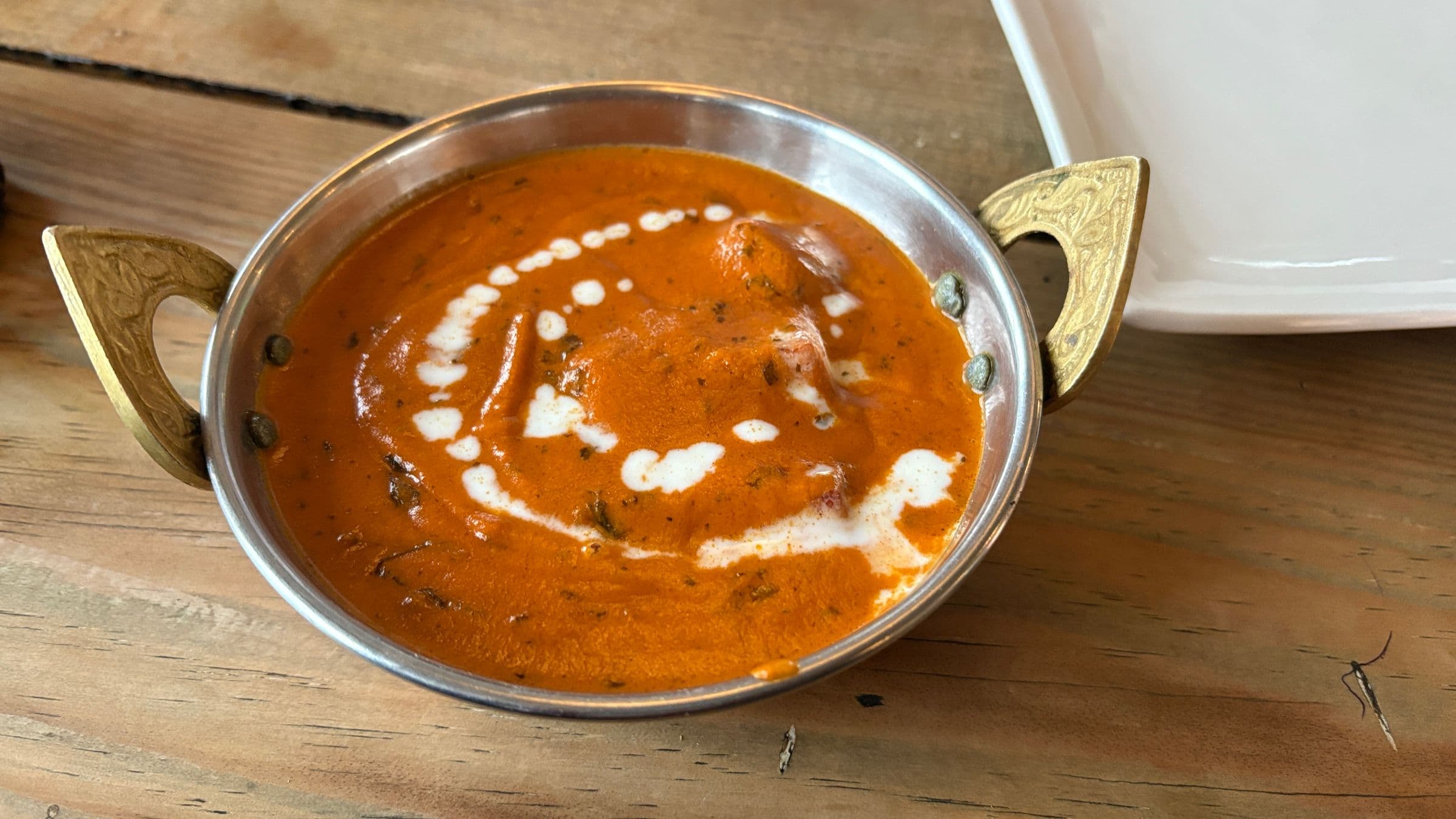 Creamy orange curry served in a steel karahi with ornate brass handles
