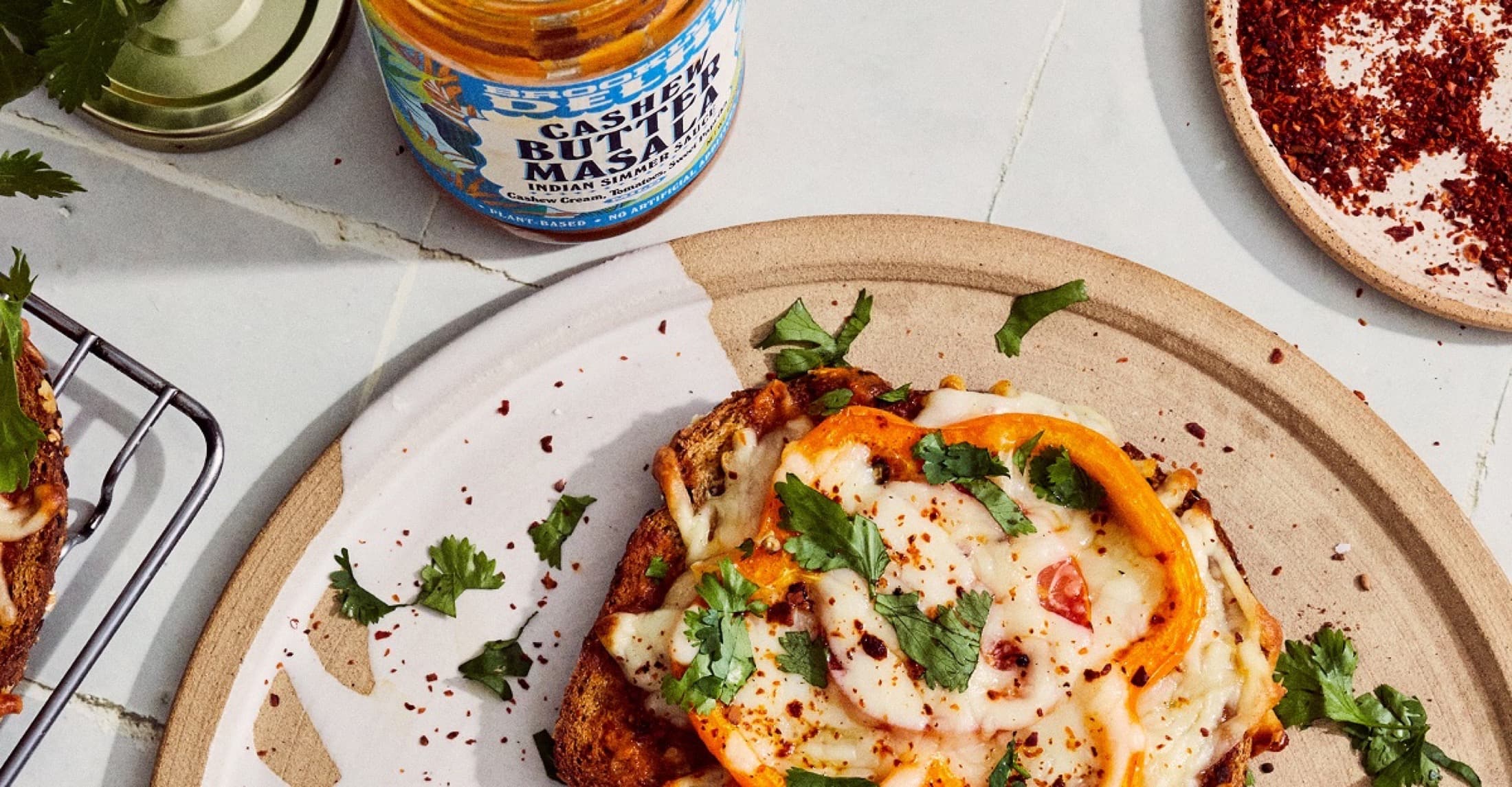 Brooklyn Delhi Cashew Butter Masala jar beside pizza toast with peppers and cilantro
