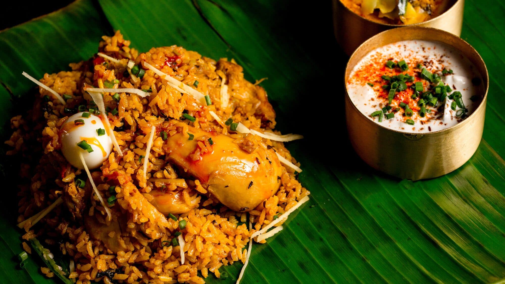 Orange-spiced rice with chicken and a boiled egg on a banana leaf, with brass bowls of raita and curry, at Bulbul in Blackfriars