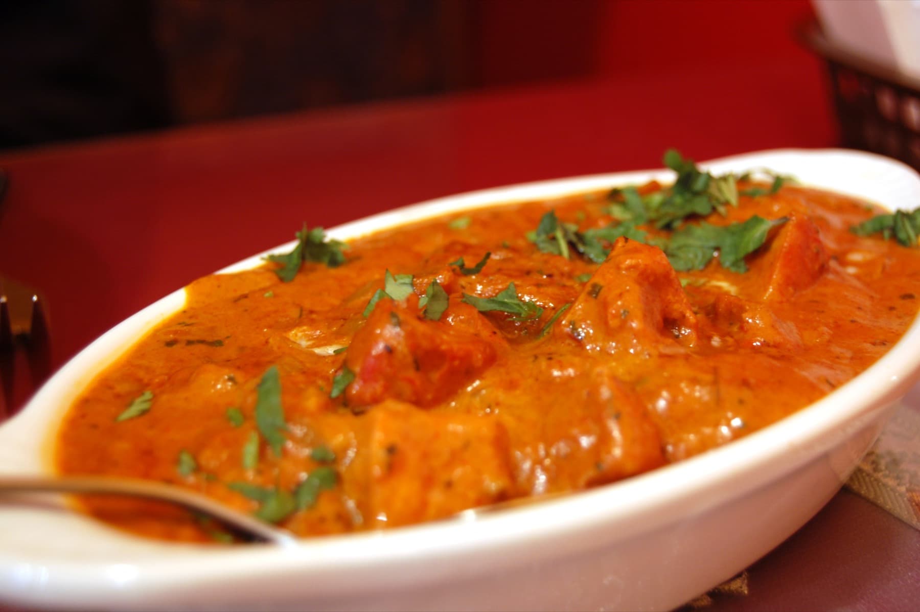 Butter chicken in a white bowl with cilantro garnish and a silver spoon