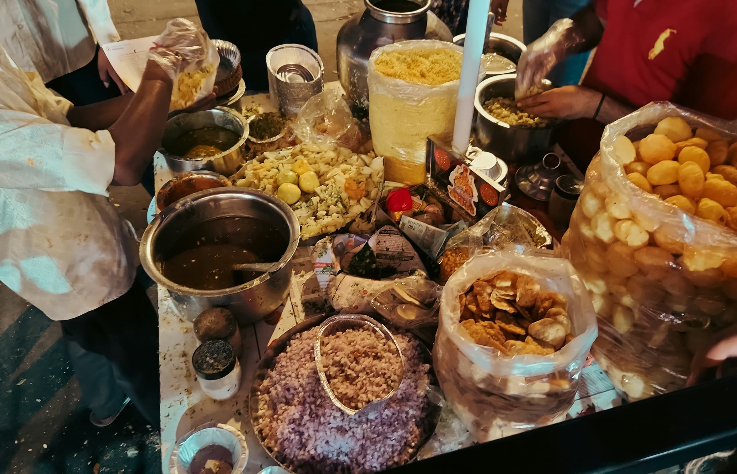 Mumbai chaat counter with puri shells, sev, potato, onions, chutneys, and vendors assembling plates