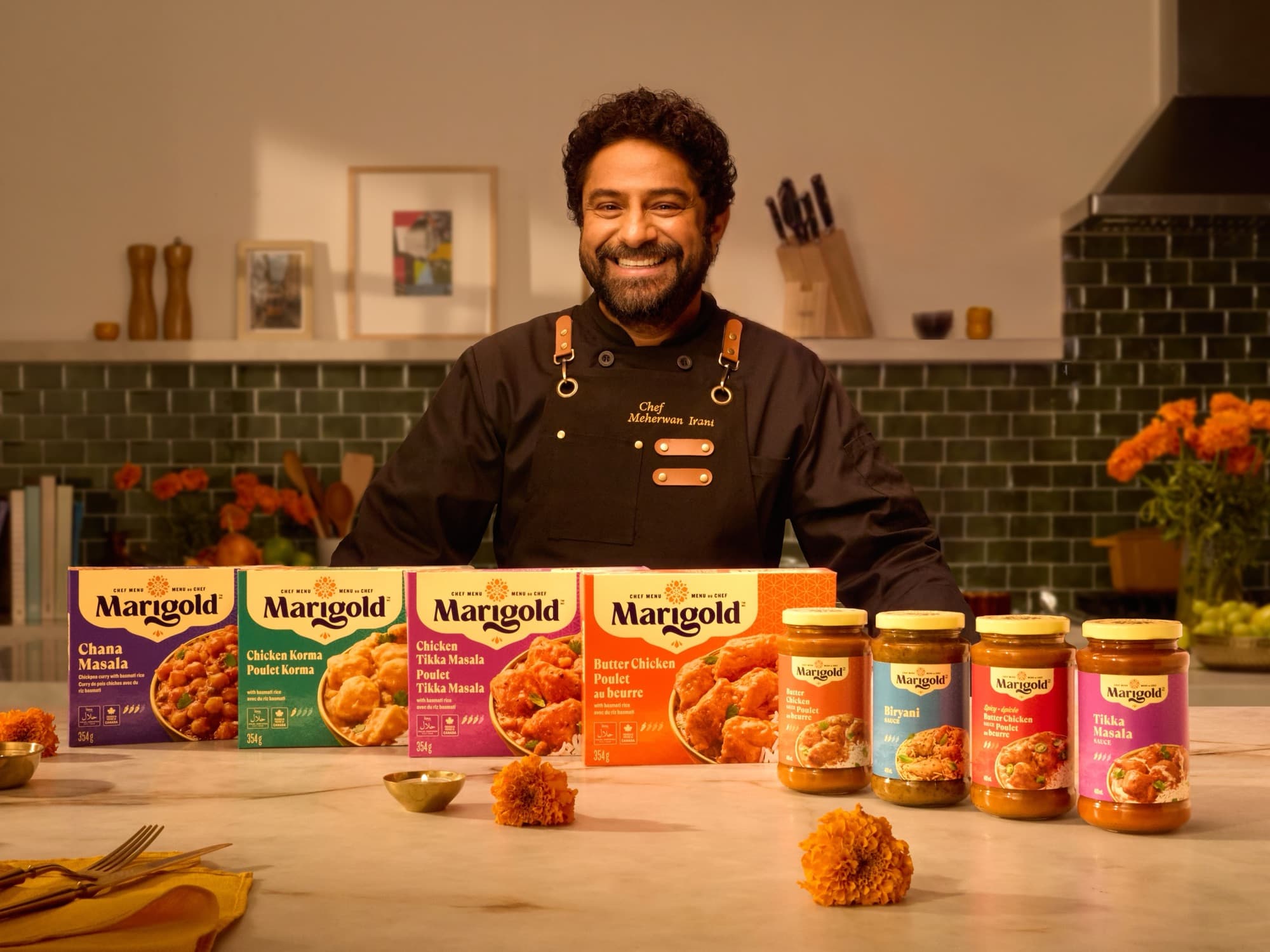 Chef Meherwan Irani behind Marigold’s four frozen meals and four cooking sauces on a kitchen counter