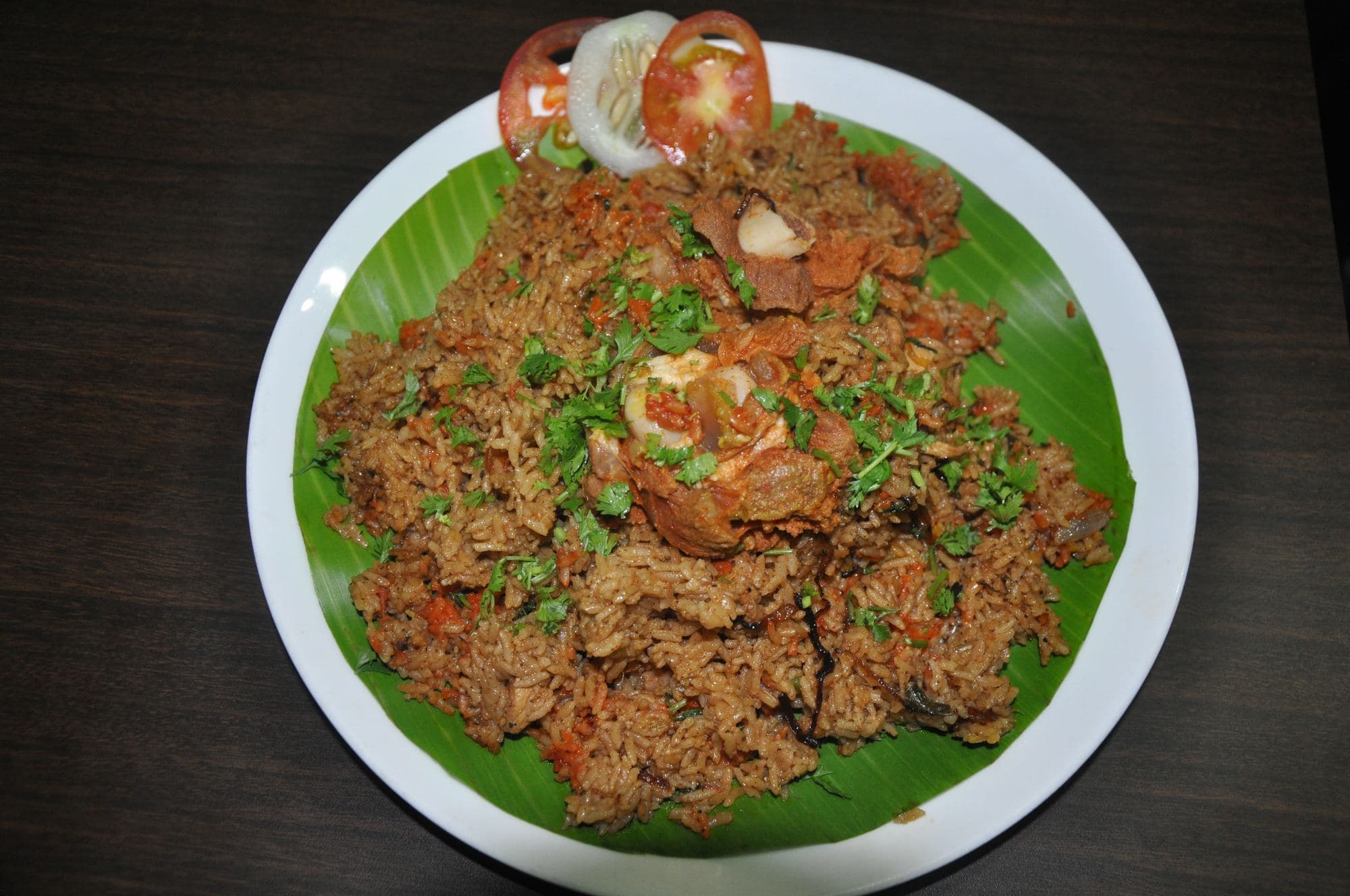 Seeraga samba mutton biryani on a banana leaf with fried onions and cilantro