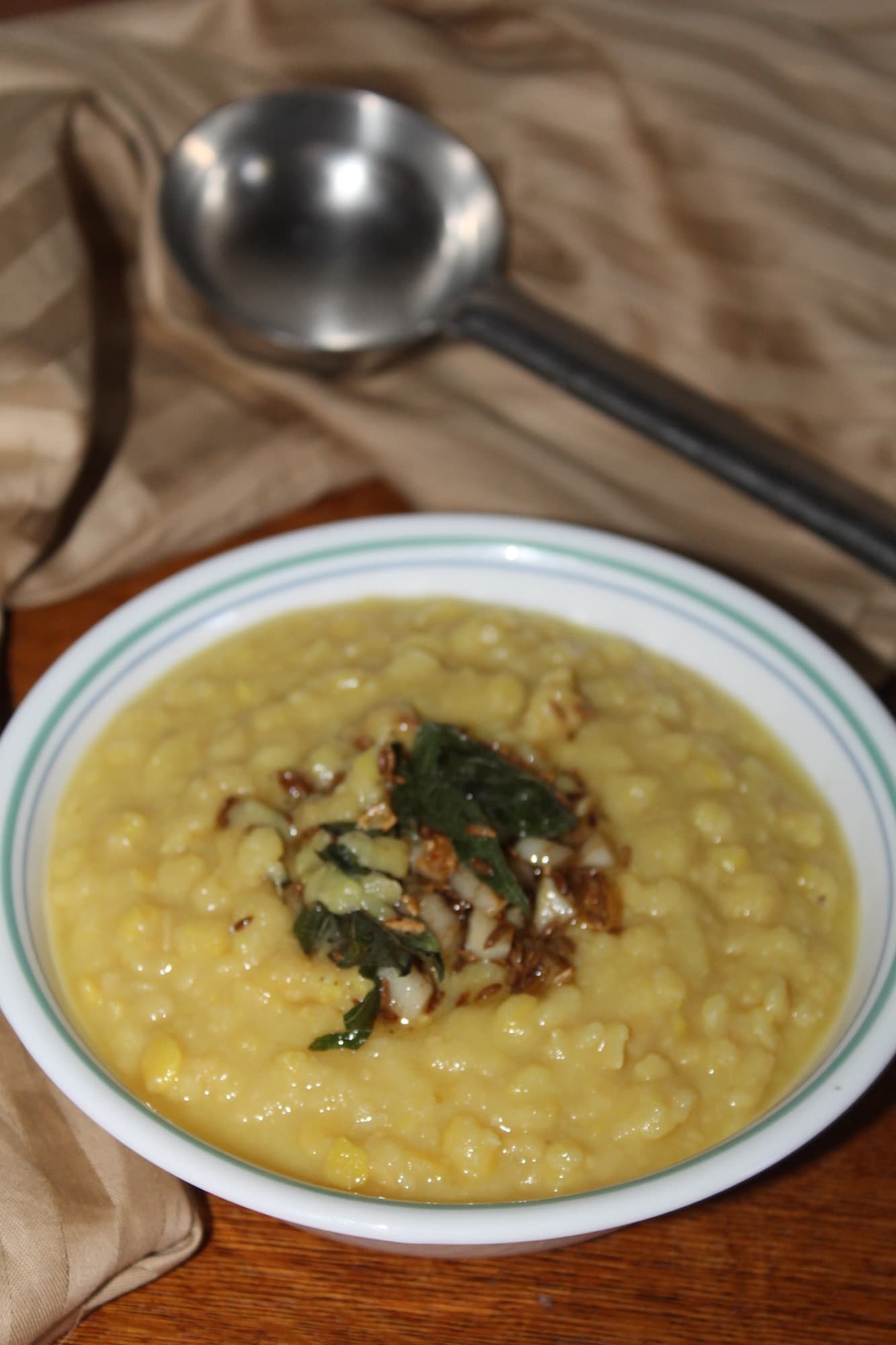 A bowl of yellow toor dal with a cumin and curry-leaf tadka, a steel ladle behind it