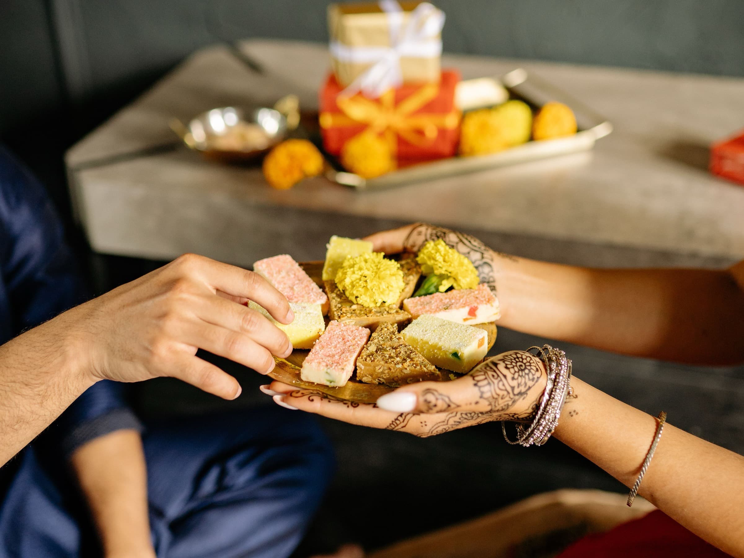Two people sharing a plate of assorted mithai during a Diwali celebration
