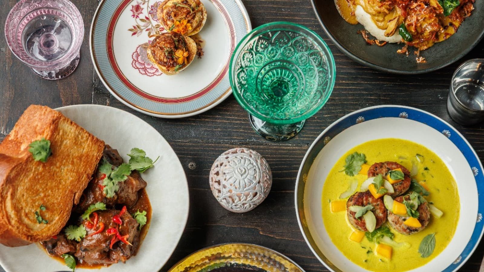 Spread of Drāvida dishes on a dark wood table, including yellow curry and braised meat with toast