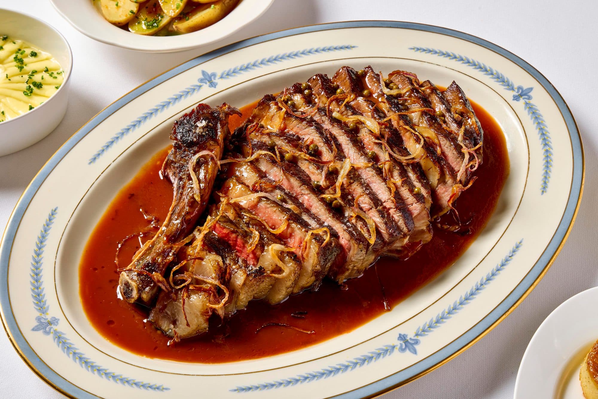 Sliced bone-in rib chop in pan juices on an oval china platter at Elder