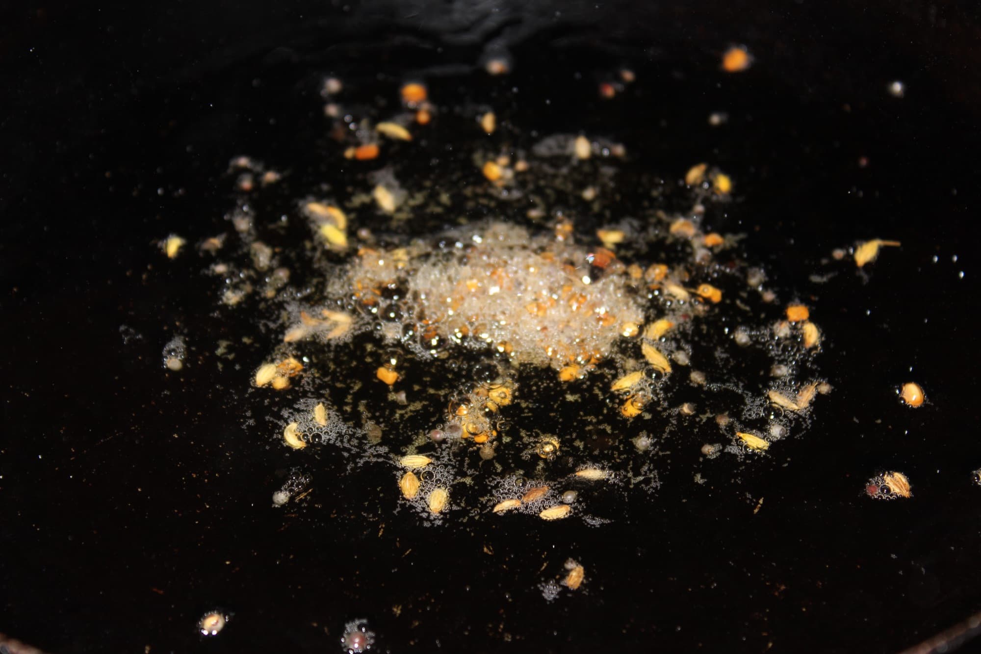 Whole spices blooming in hot oil in a dark pan during tempering