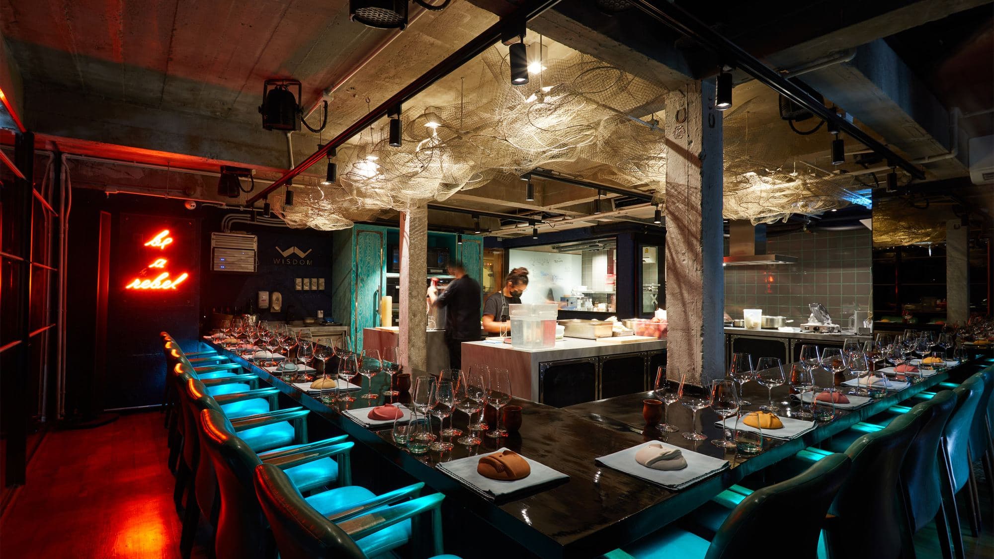 The chef’s counter at Gaggan in Bangkok, turquoise chairs under neon and a “be a rebel” sign