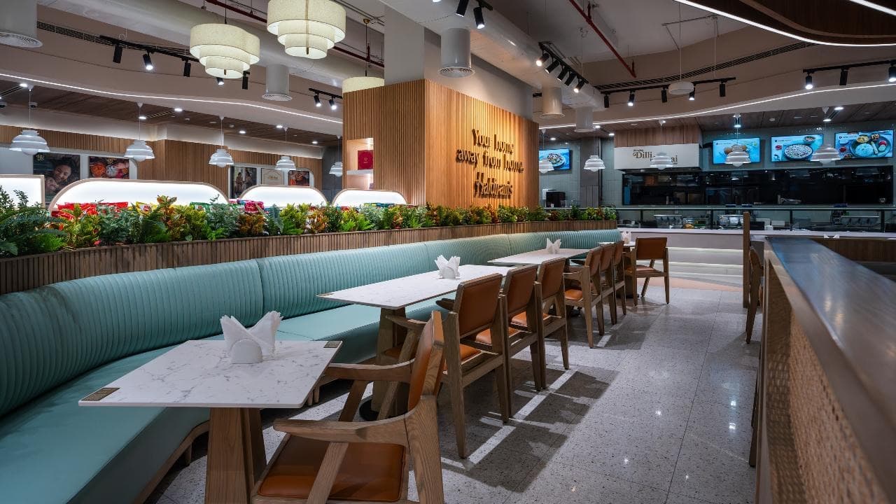 Haldiram’s Dubai dining room with a mint banquette, marble tables, and a wood wall reading Your home away from home
