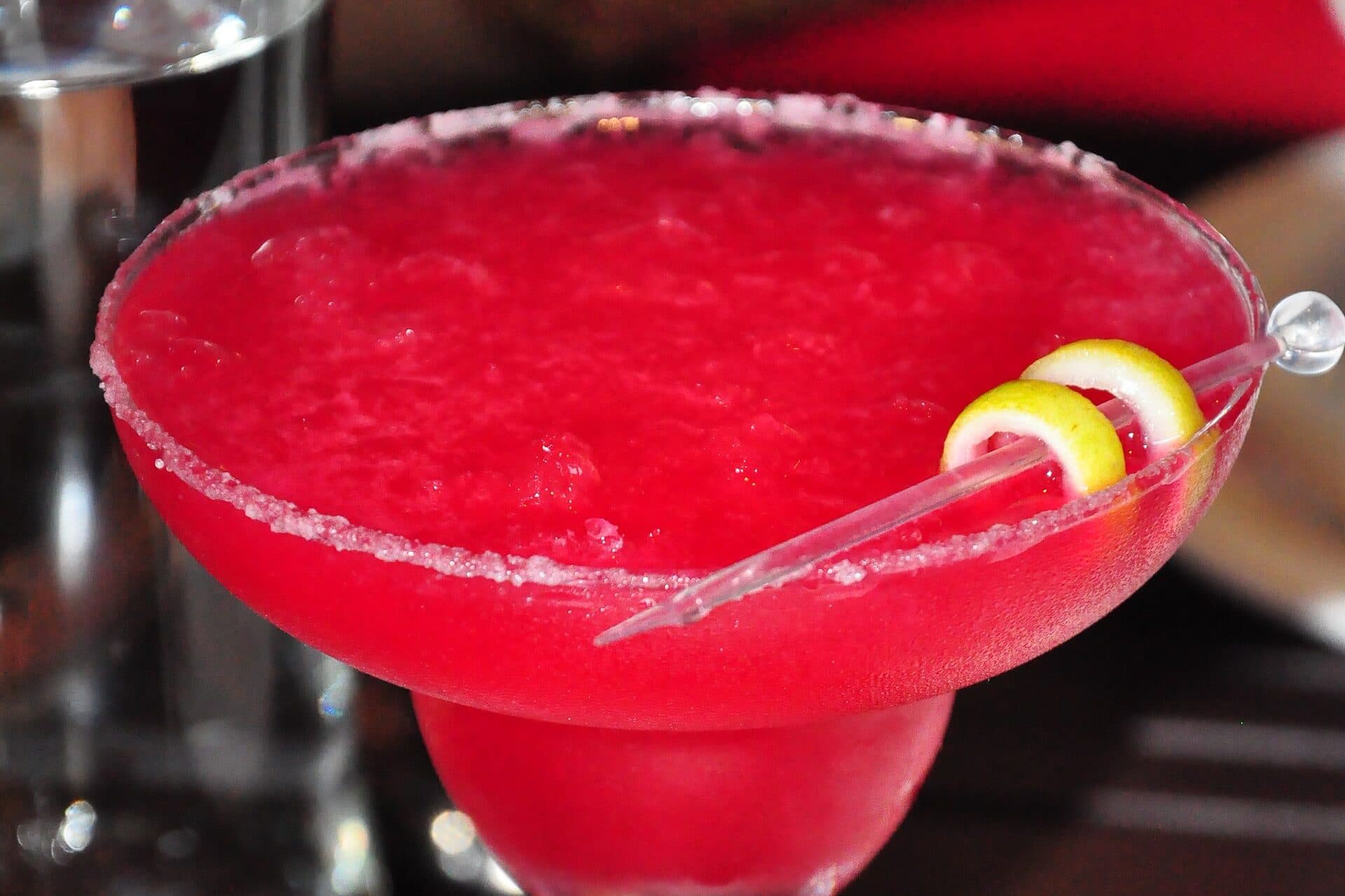 Bright pink frozen raspberry margarita in a salted-rim glass with citrus twists