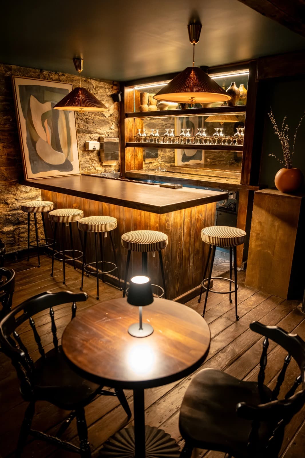 The downstairs lounge at Jam & Jaggery: a small wooden bar with striped stools, pendant lamps, and a round table with a lamp