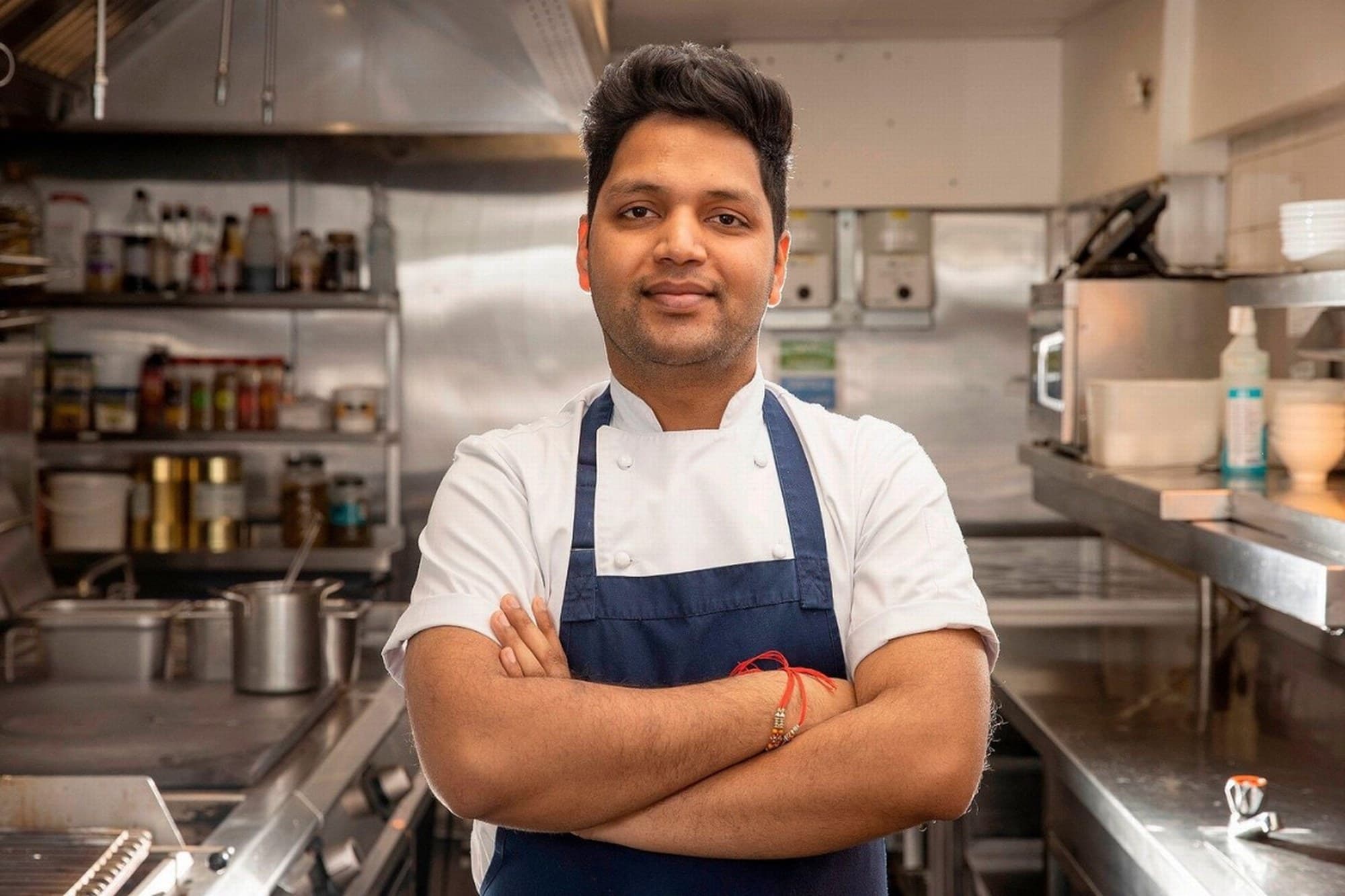 Chef Sagar Massey in a white jacket and navy apron in a commercial kitchen