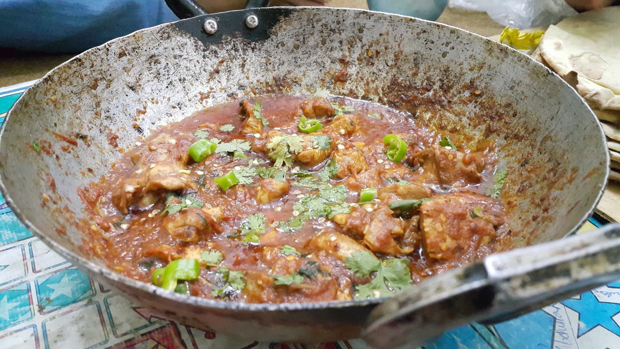 Chicken karahi in a worn steel pot, finished with cilantro and green chili