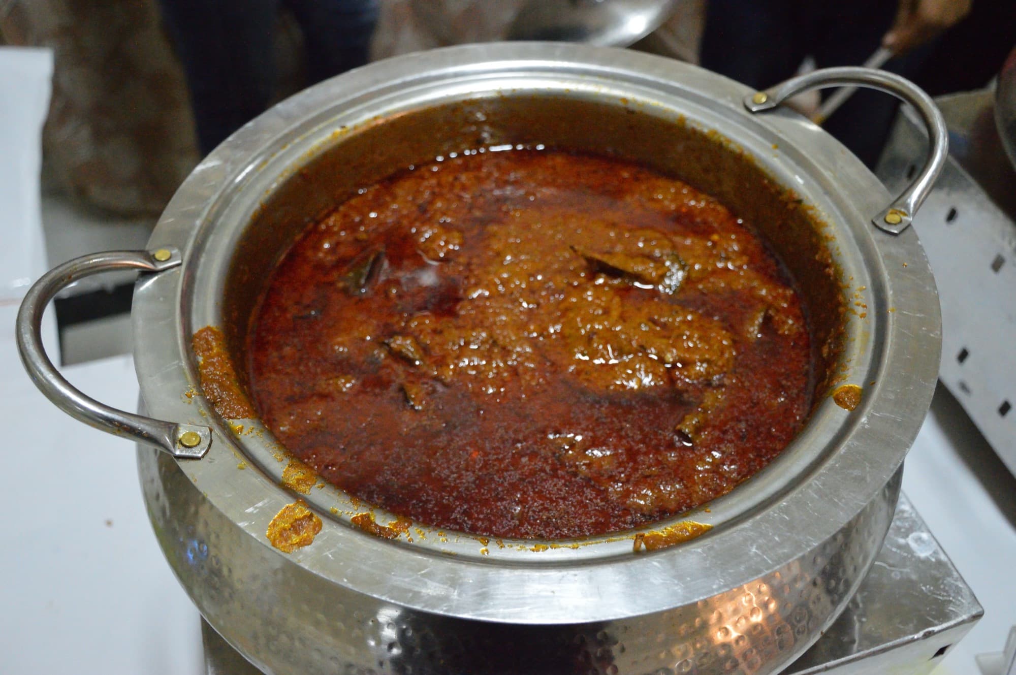 Mutton rogan josh in a metal pot, deep red gravy with oil on the surface