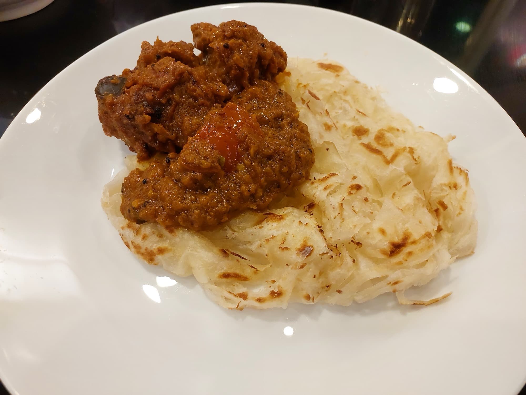 Layered Kerala parotta pulled open beside a dark meat roast