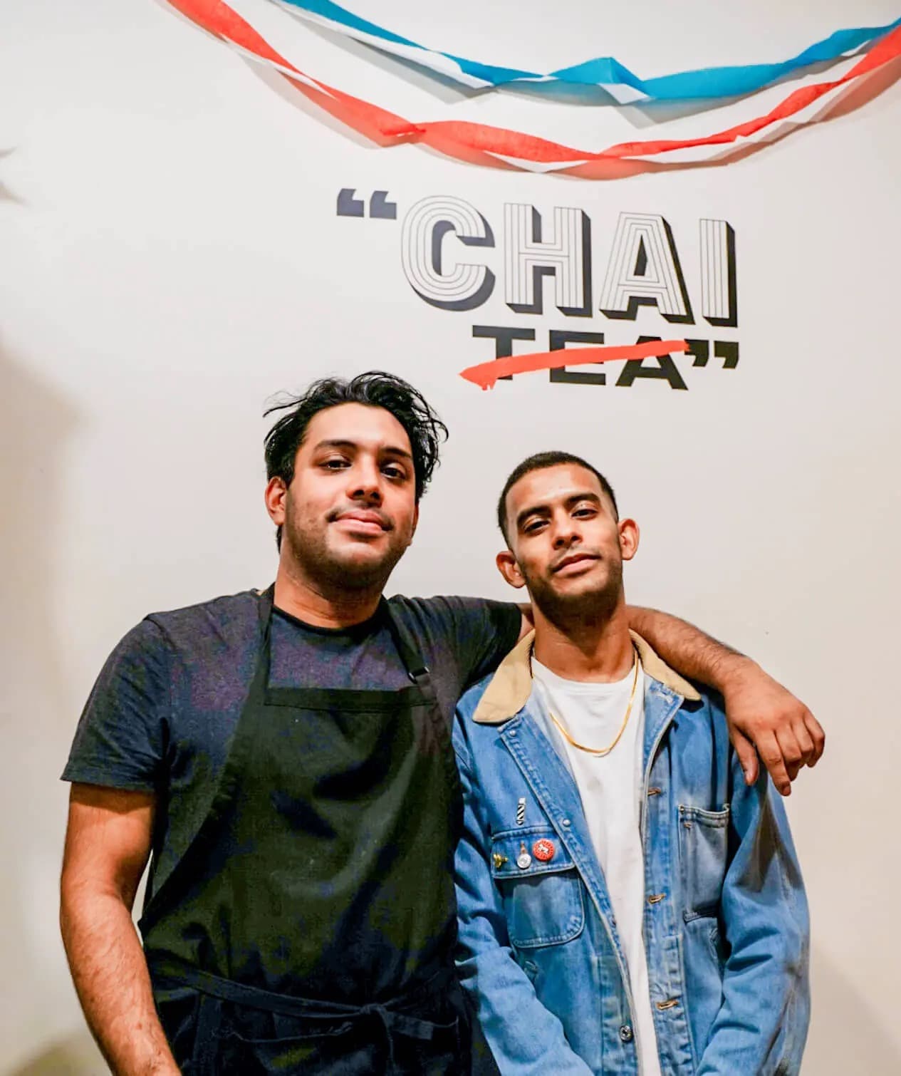 Kolkata Chai Co. founders Ani and Ayan Sanyal under a wall graphic that crosses out TEA in CHAI TEA