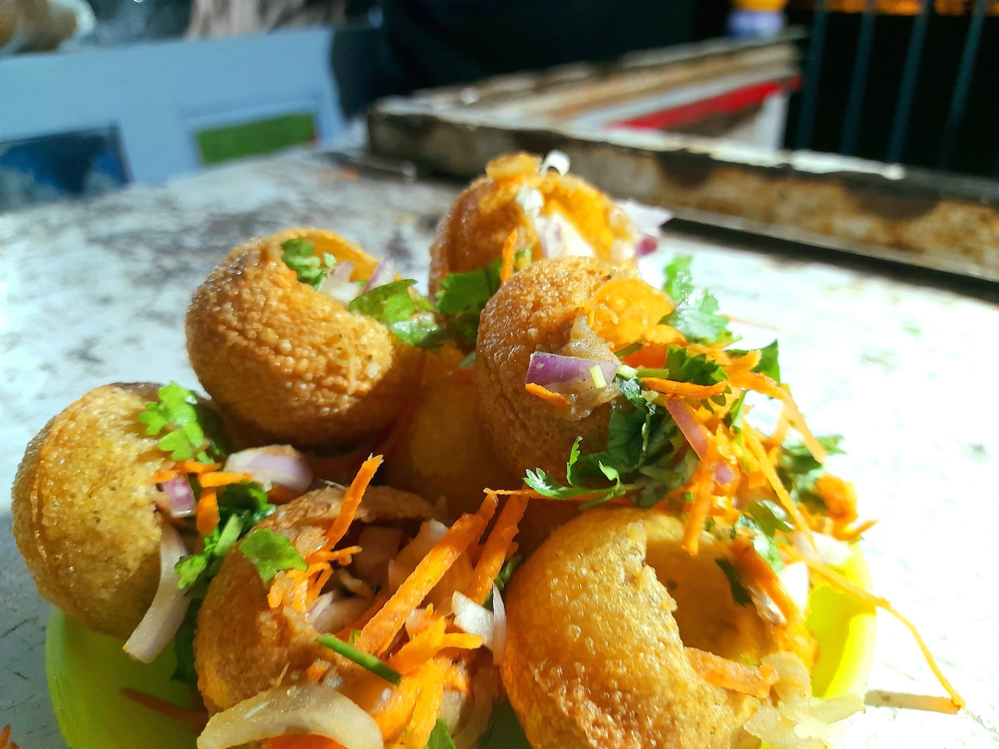 Fried phuchka shells split open and topped with onion, carrot, and coriander