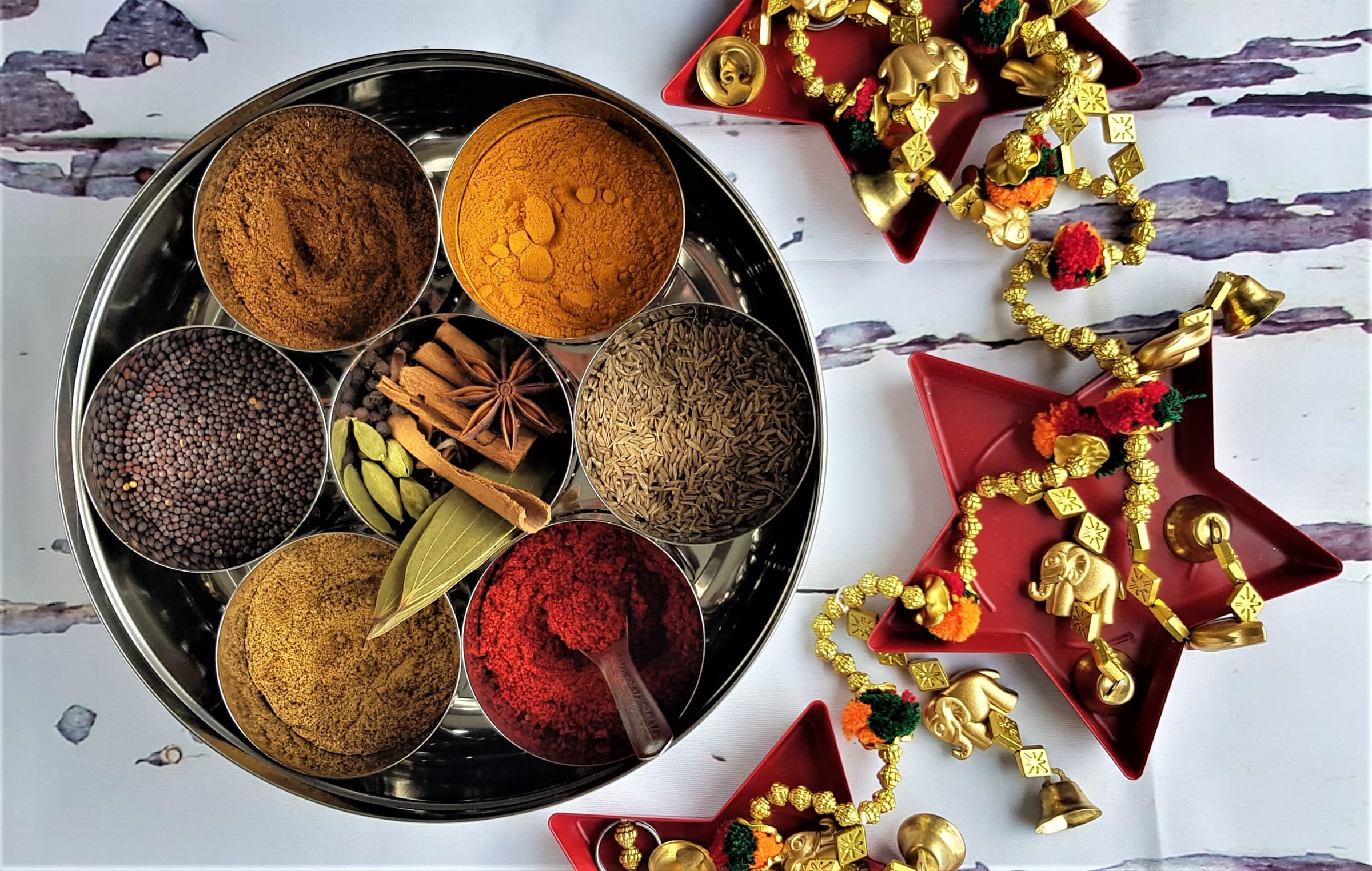 Open stainless steel masala dabba with seven cups of colorful whole and ground spices