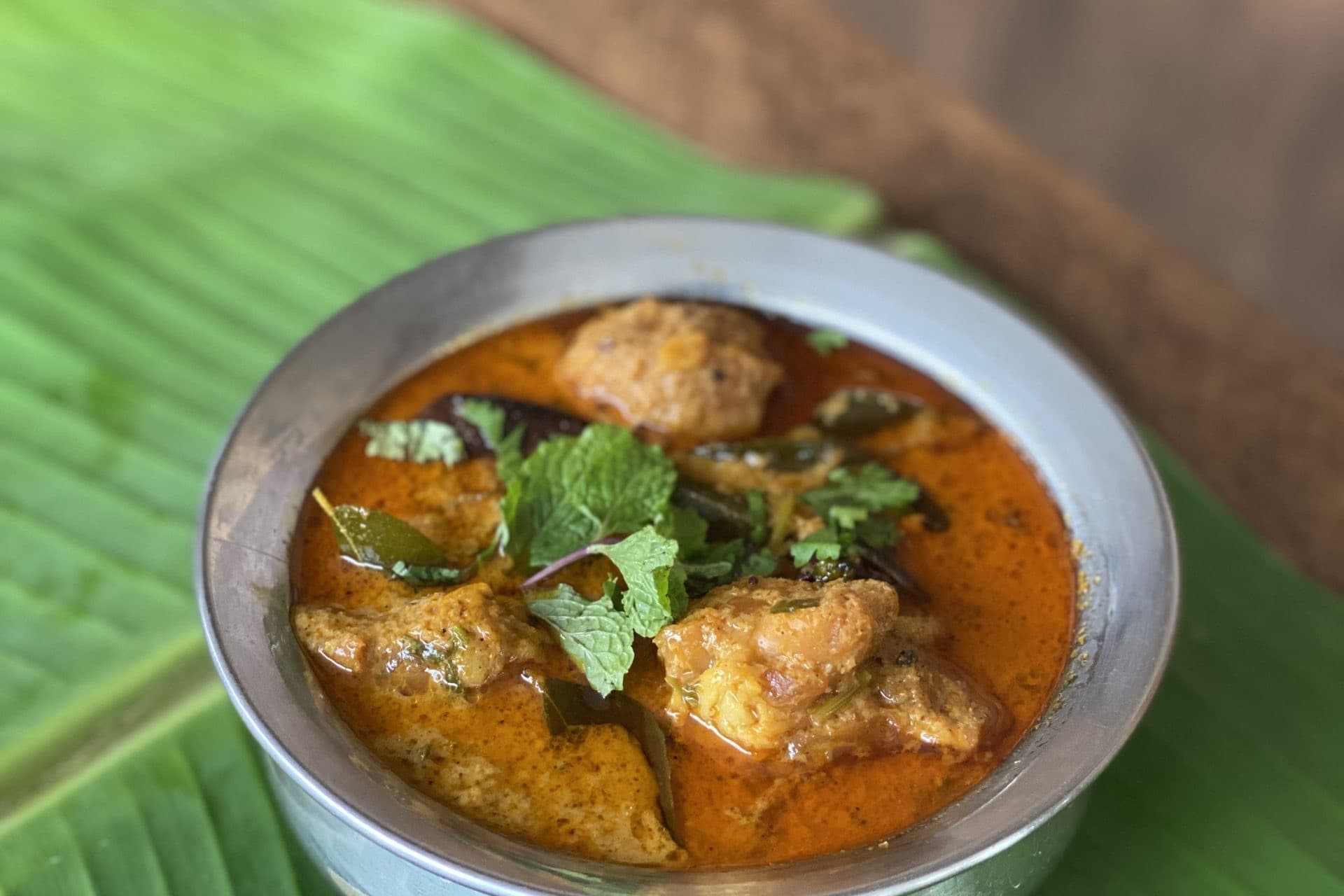Andhra chicken curry in a steel bowl with mint and coriander, set on a banana leaf