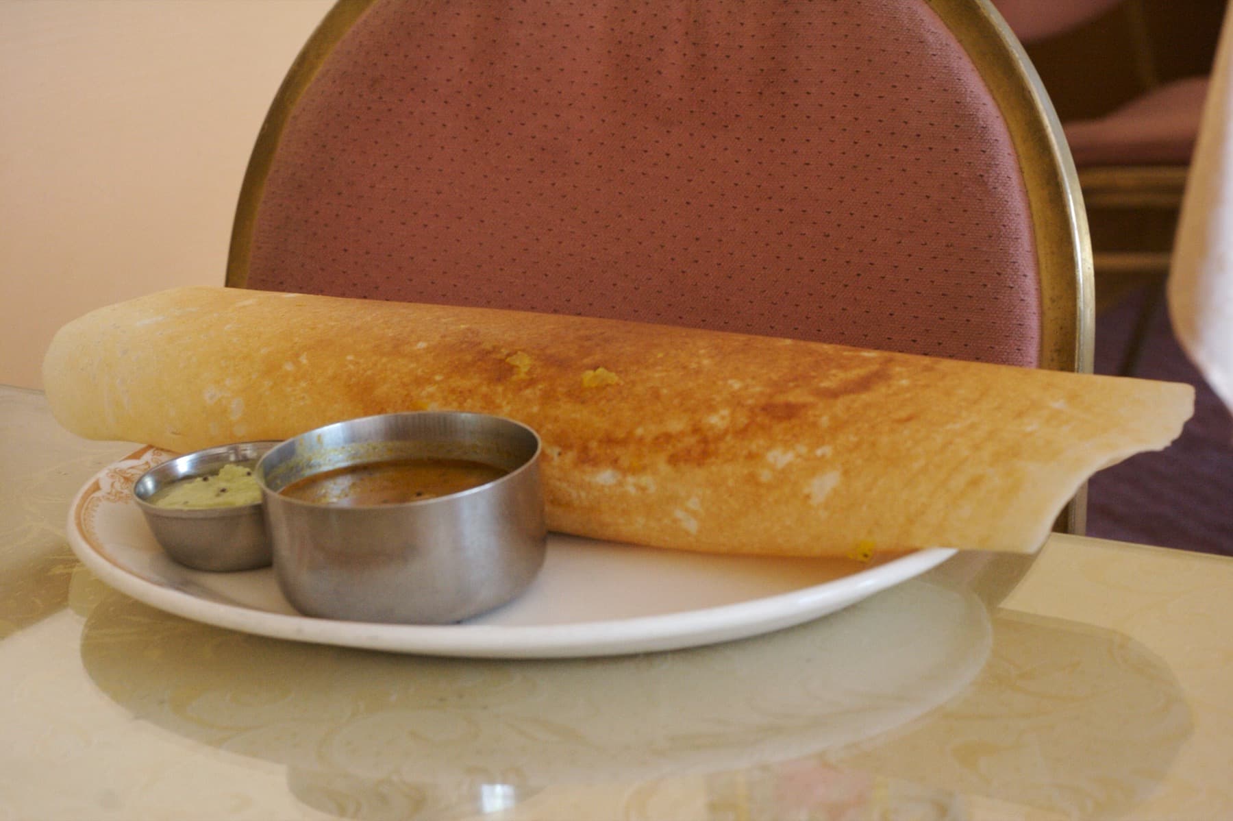 Crispy dosa on a plate with coconut chutney and a bowl of sambar