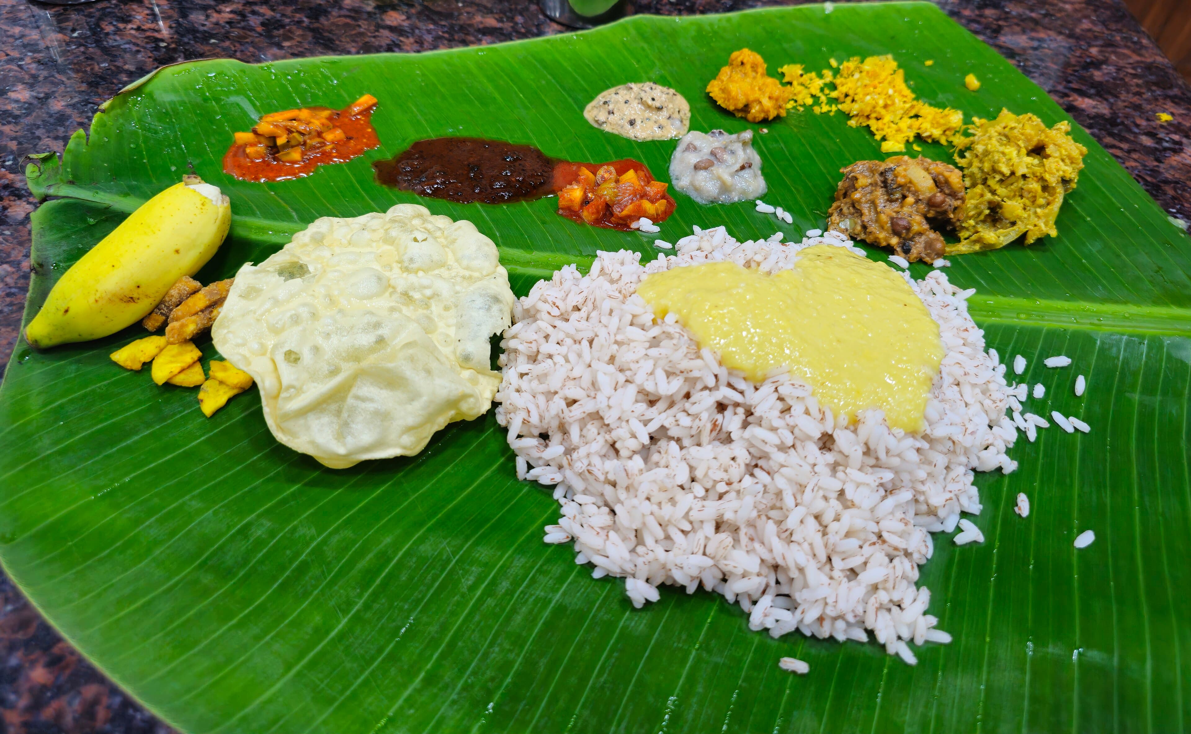 Onam sadya with rice, parippu, vegetable dishes, pickles, banana, chips, and pappadam on a banana leaf