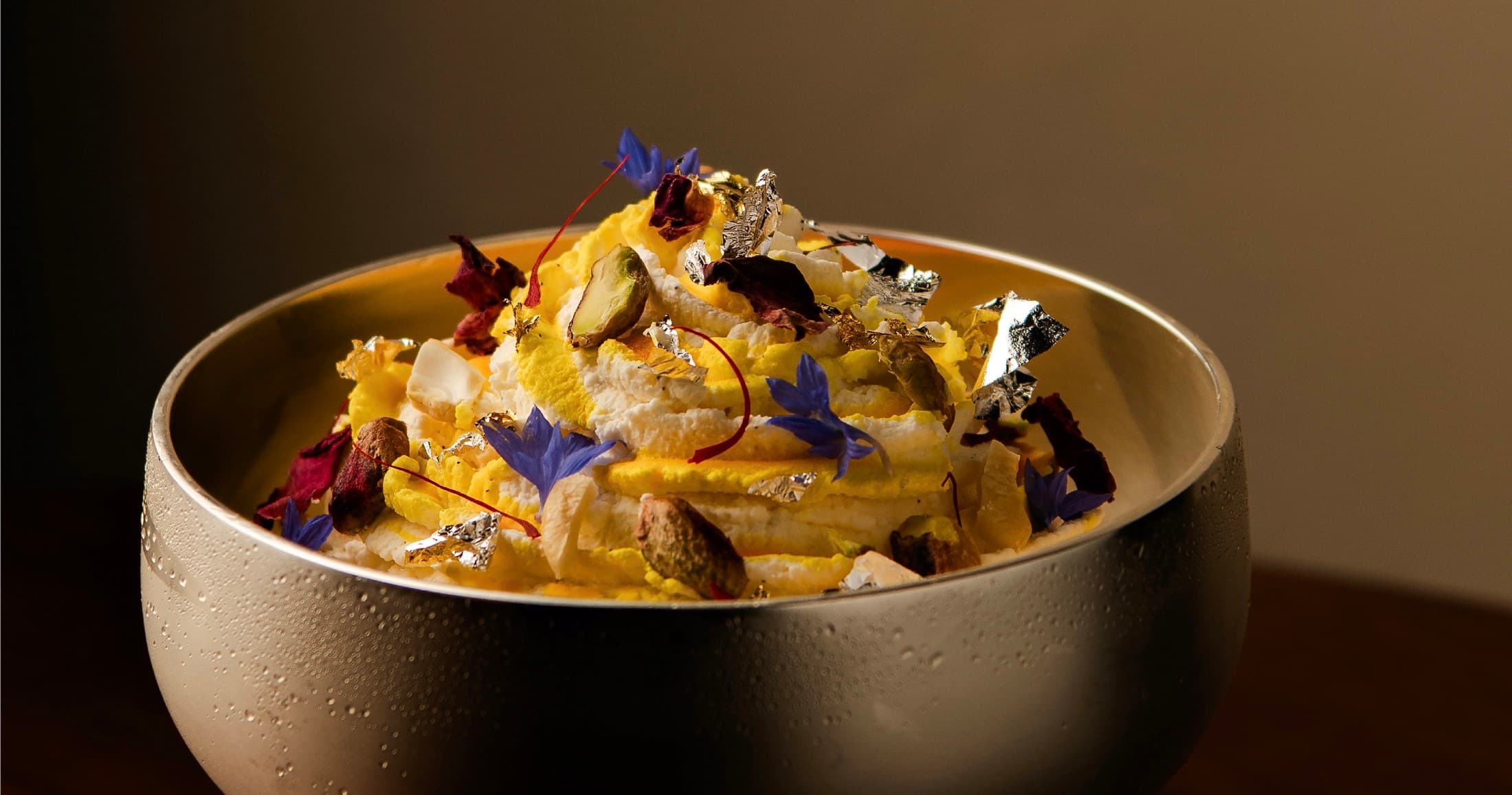 Chilled Awadhi milk foam dessert with silver leaf, pistachios, and edible flowers at Oudh 1722
