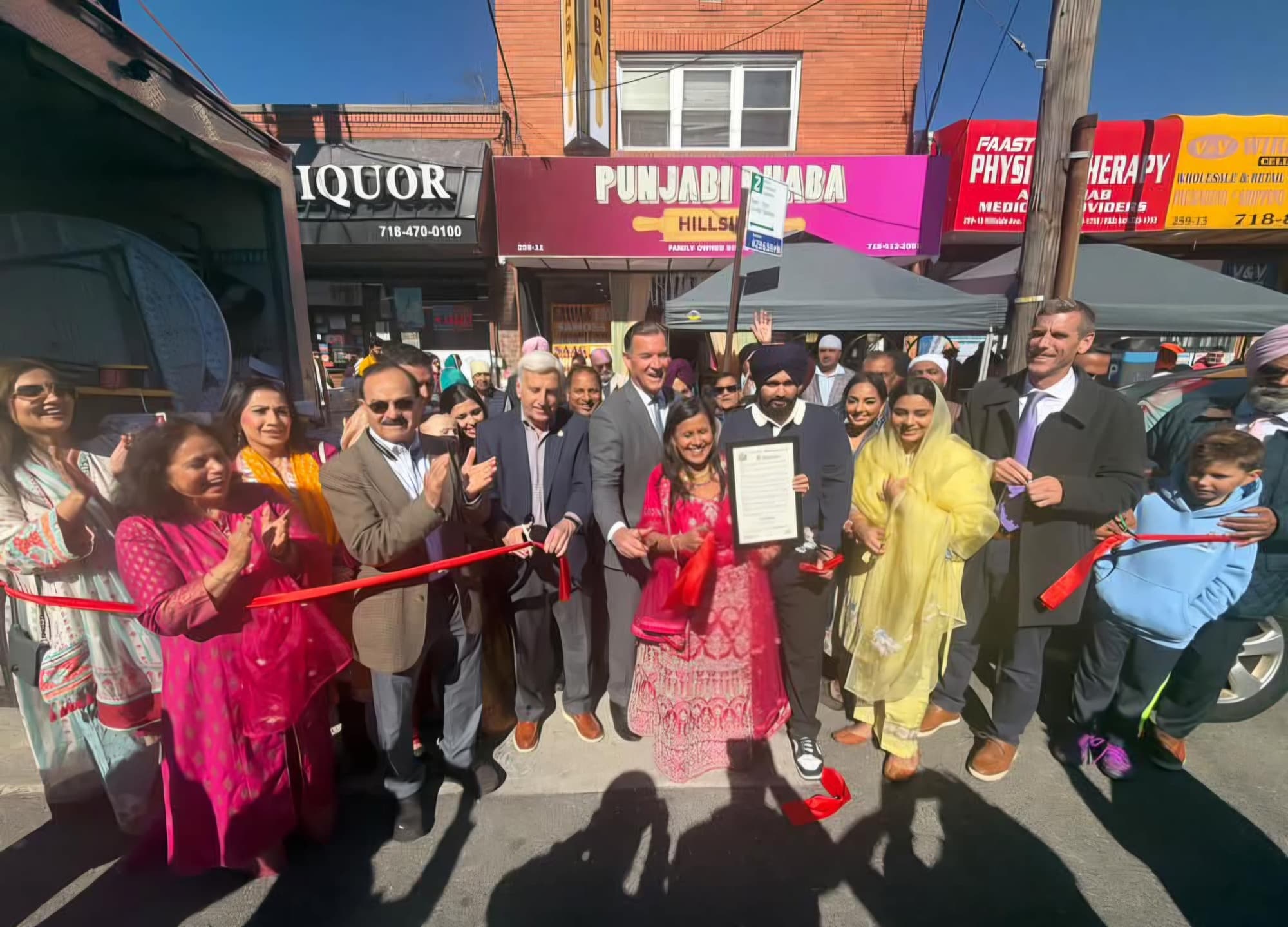 A ribbon cutting outside Punjabi Dhaba on Hillside Avenue in Glen Oaks, with the restaurant sign above the door