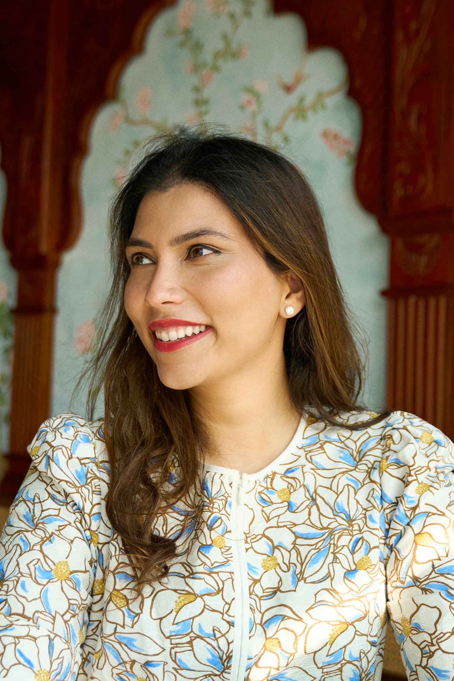 Ambica Jain smiling in a cream floral blouse under a carved wooden arch at Adrak