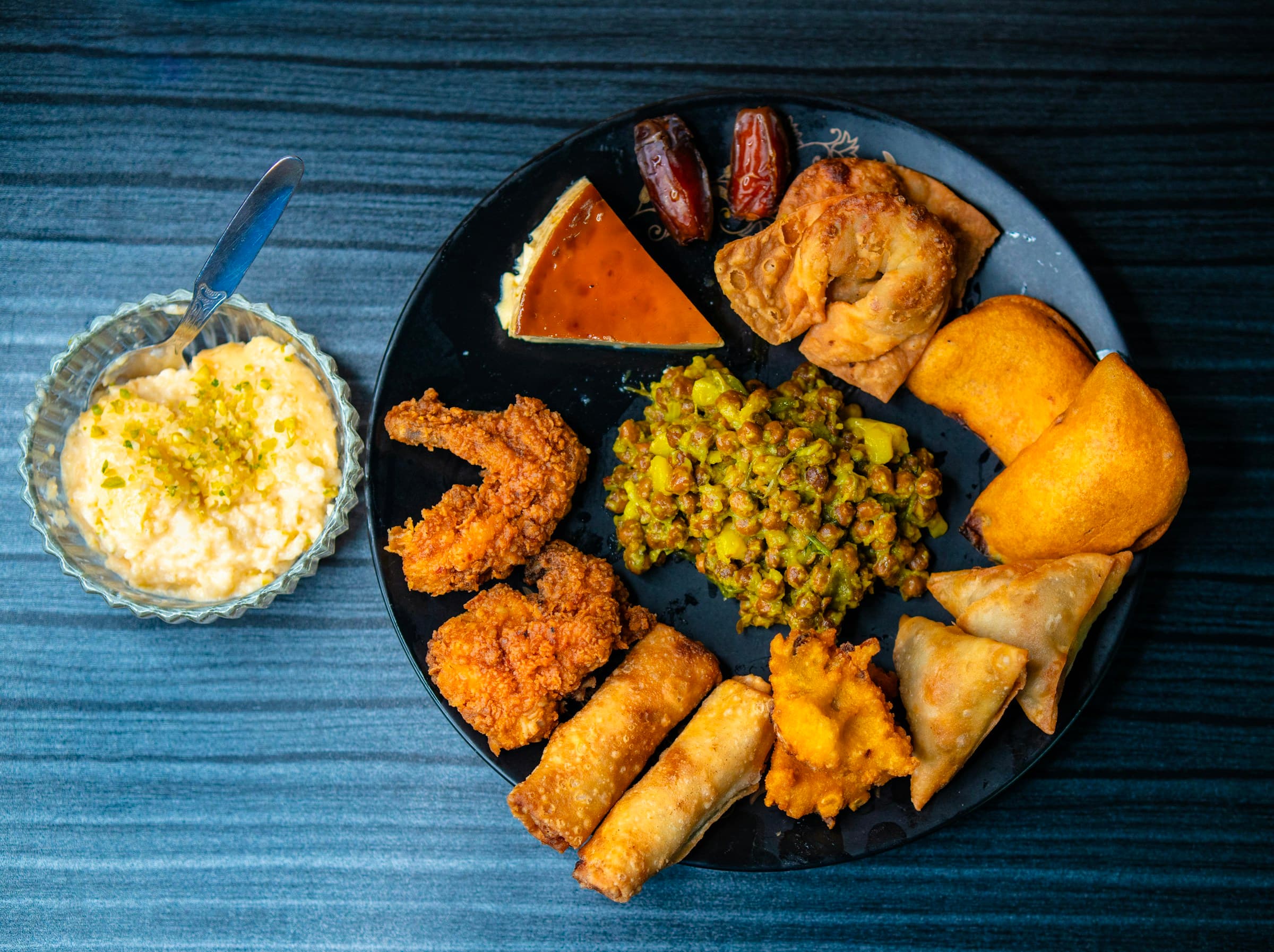 Bangladeshi iftar platter with dates, chola, samosas, fritters, rolls, and a sweet dish