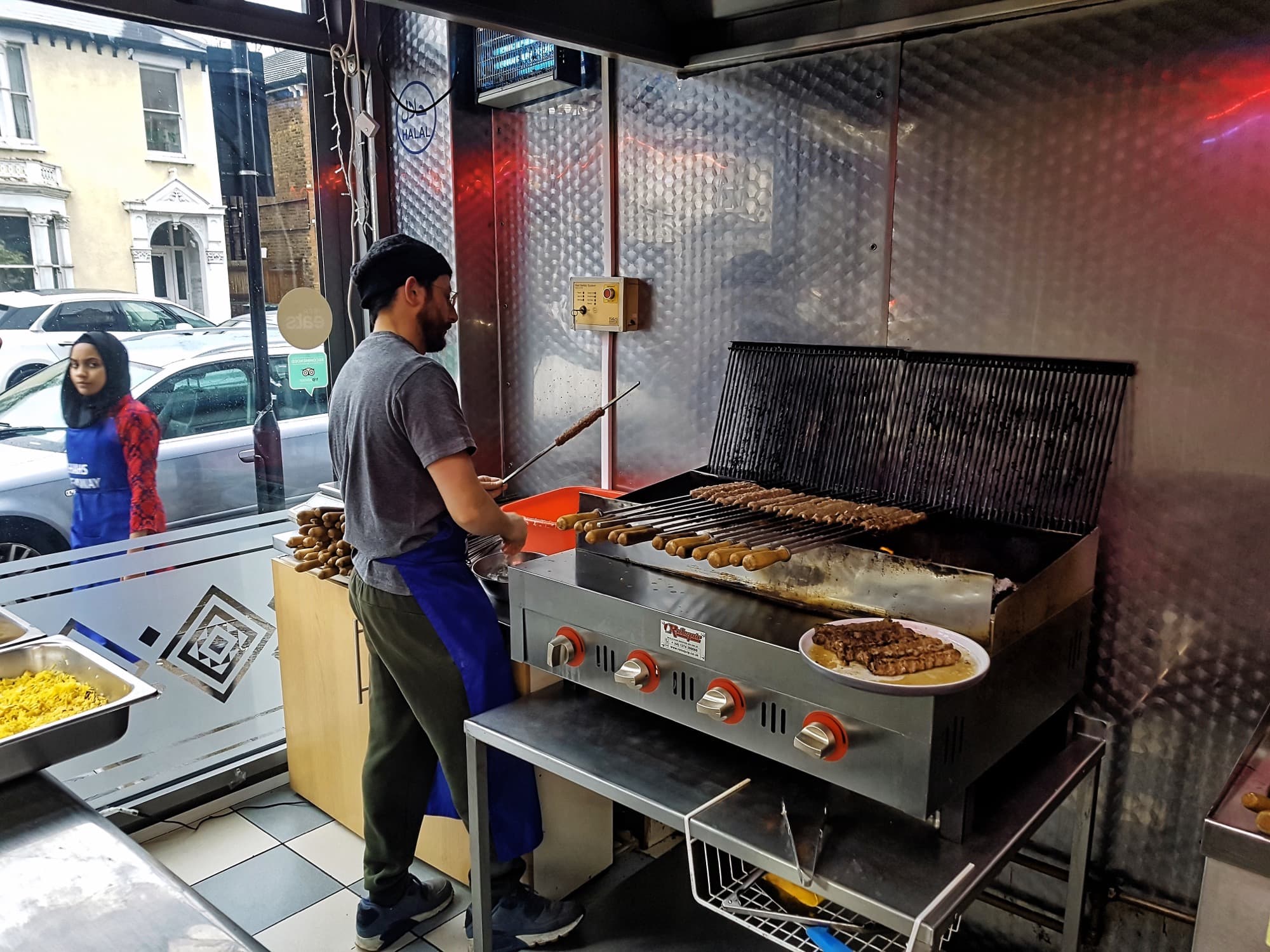 Cook preparing and grilling seekh kebabs at a London takeaway kitchen