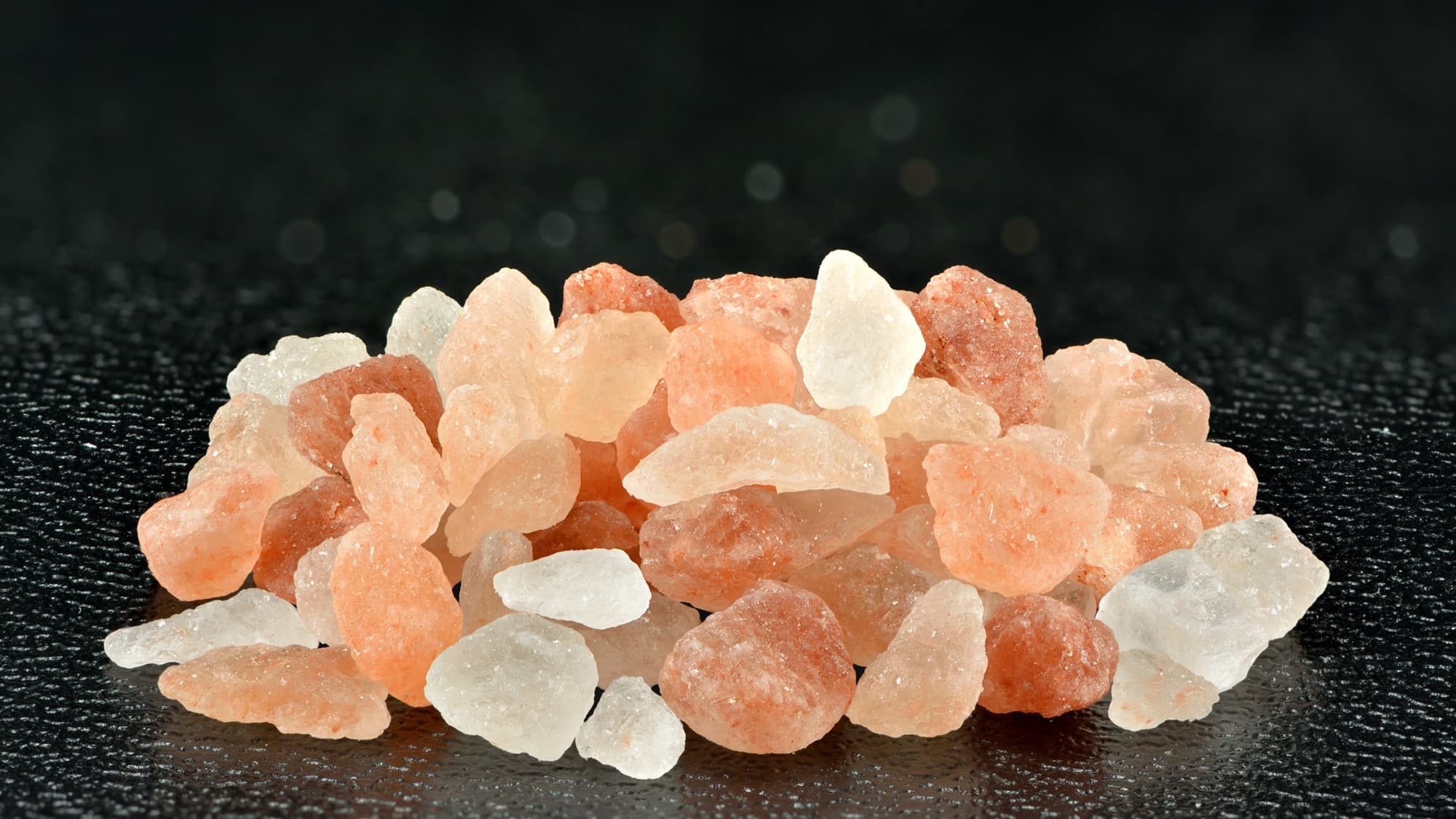Pile of coarse Himalayan rock salt crystals in shades of white, pink, and terracotta on a dark surface