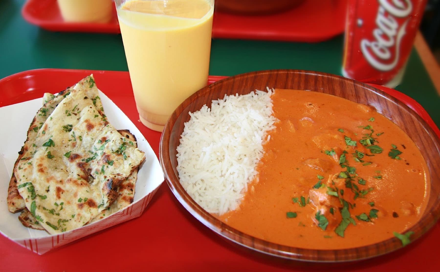 Chicken tikka masala with rice, naan, and mango lassi on a red takeaway tray