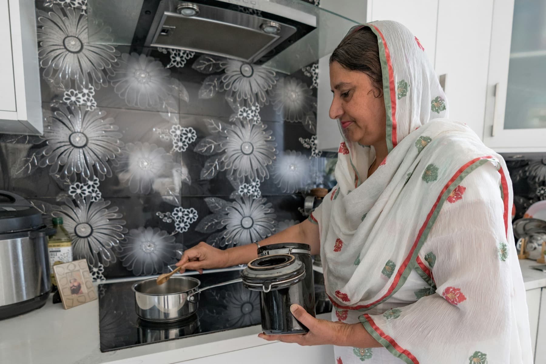 A South Asian woman in a white salwar kameez stirring a pot on a modern kitchen stove