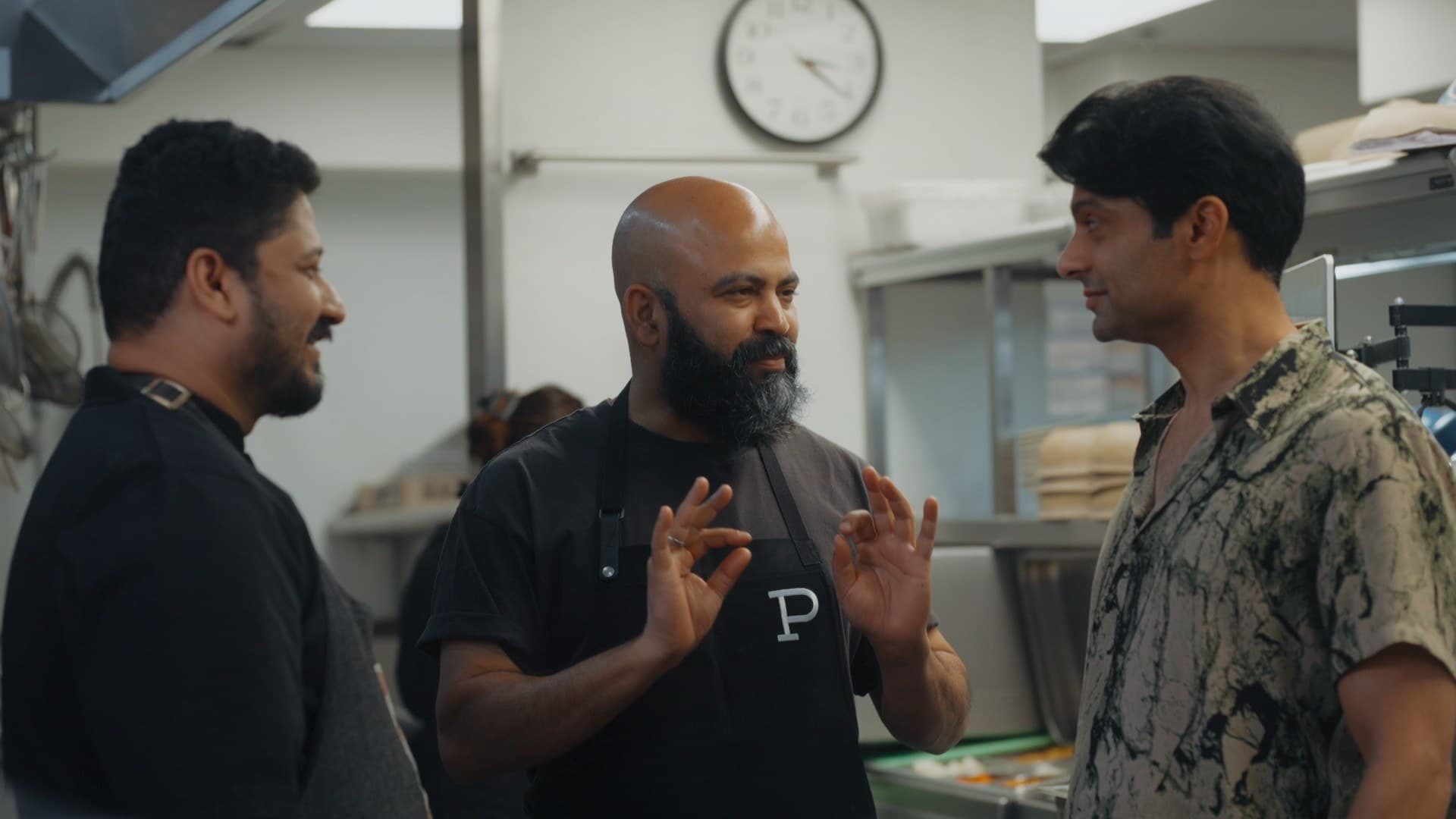 Spice Road host Rupak Ginn talks with chefs in a stainless-steel kitchen during Season 2 filming