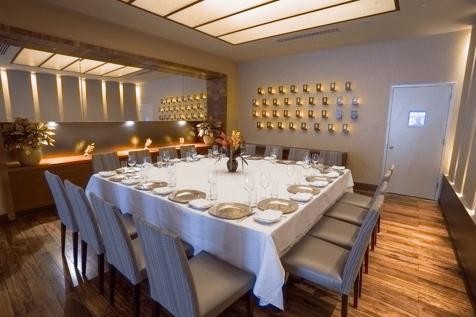 A private dining table at Tamarind in Tribeca, set with silver chargers and striped chairs under a wall of small lights