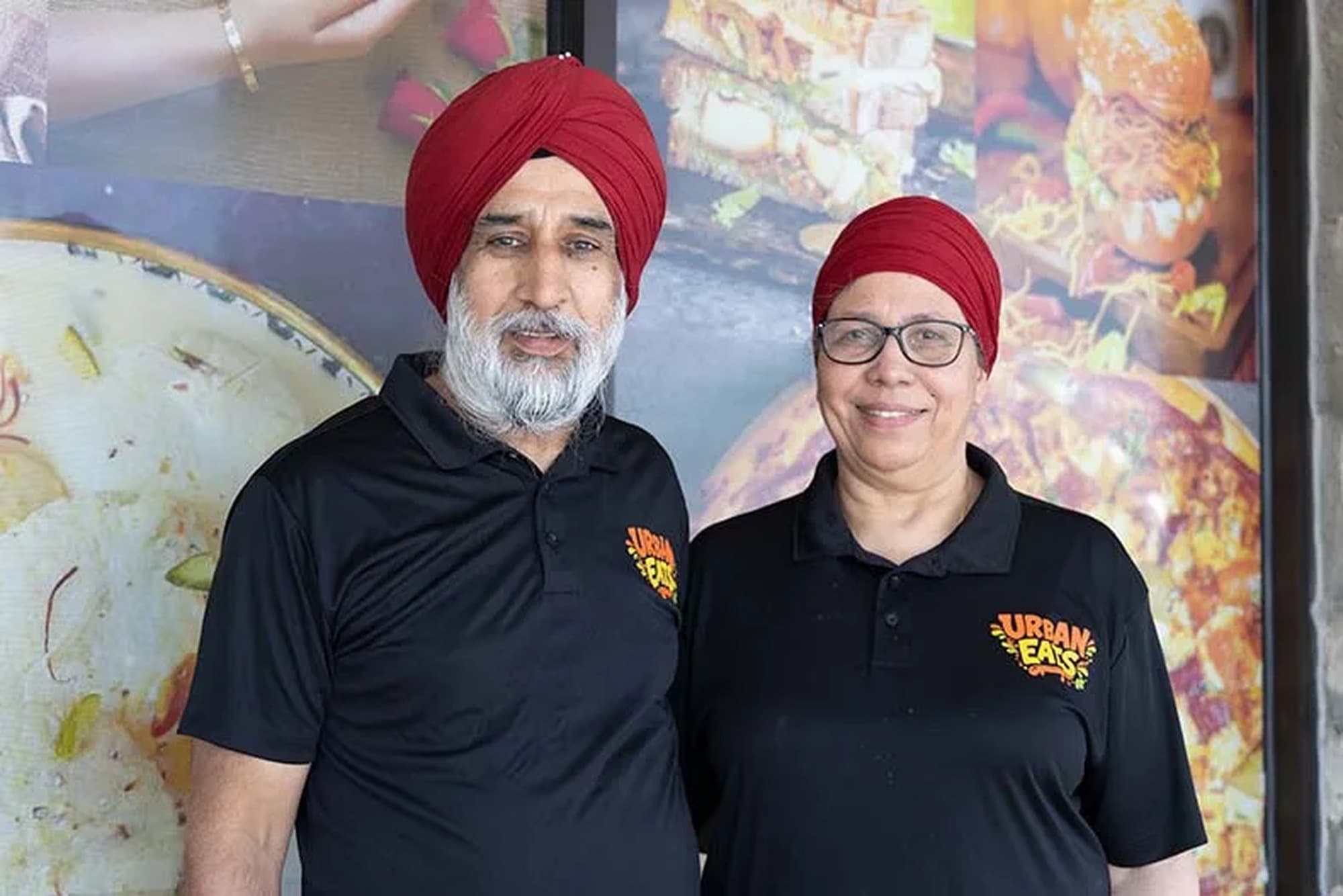 Jaspal Singh and Manjit Kaur in Urban Eats polos smiling in front of a food mural