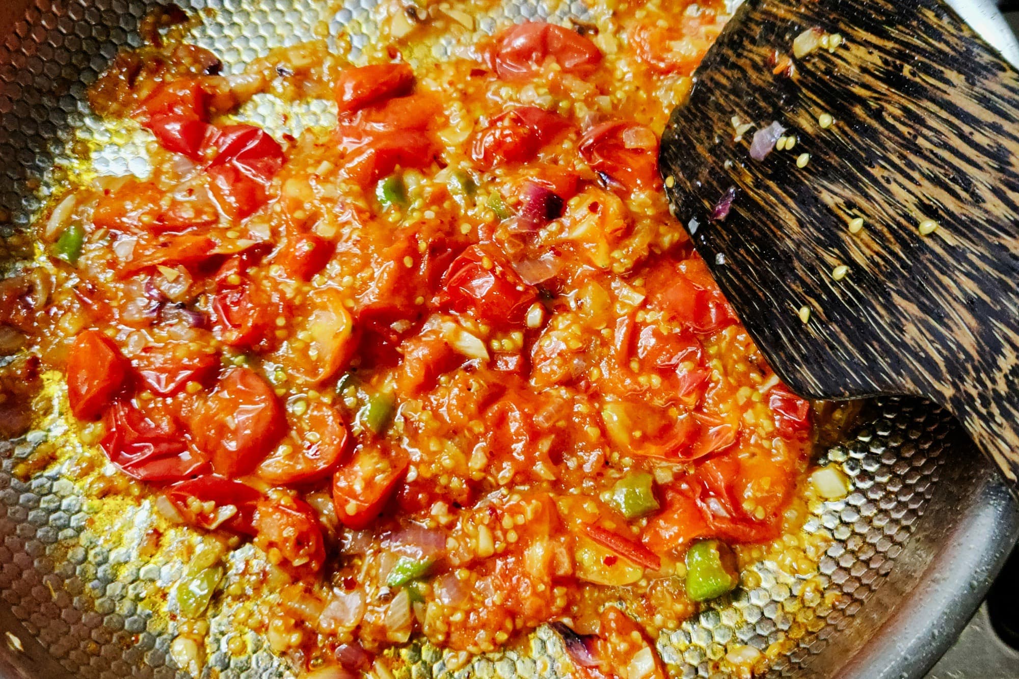 Chopped onions, tomatoes, green chilli, and spices cooking down in a wide metal pan