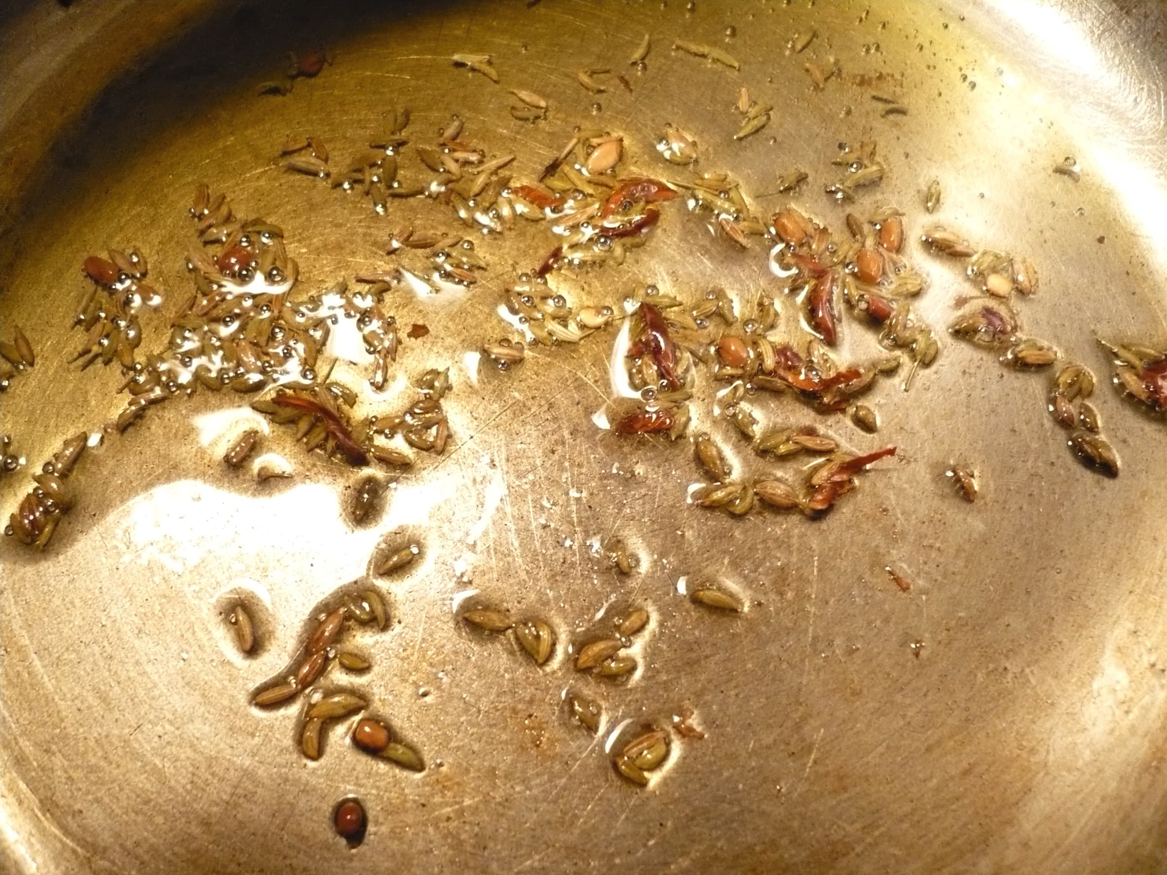 Cumin, mustard seeds, dried chili, and lentils tempering in hot oil in a metal pan